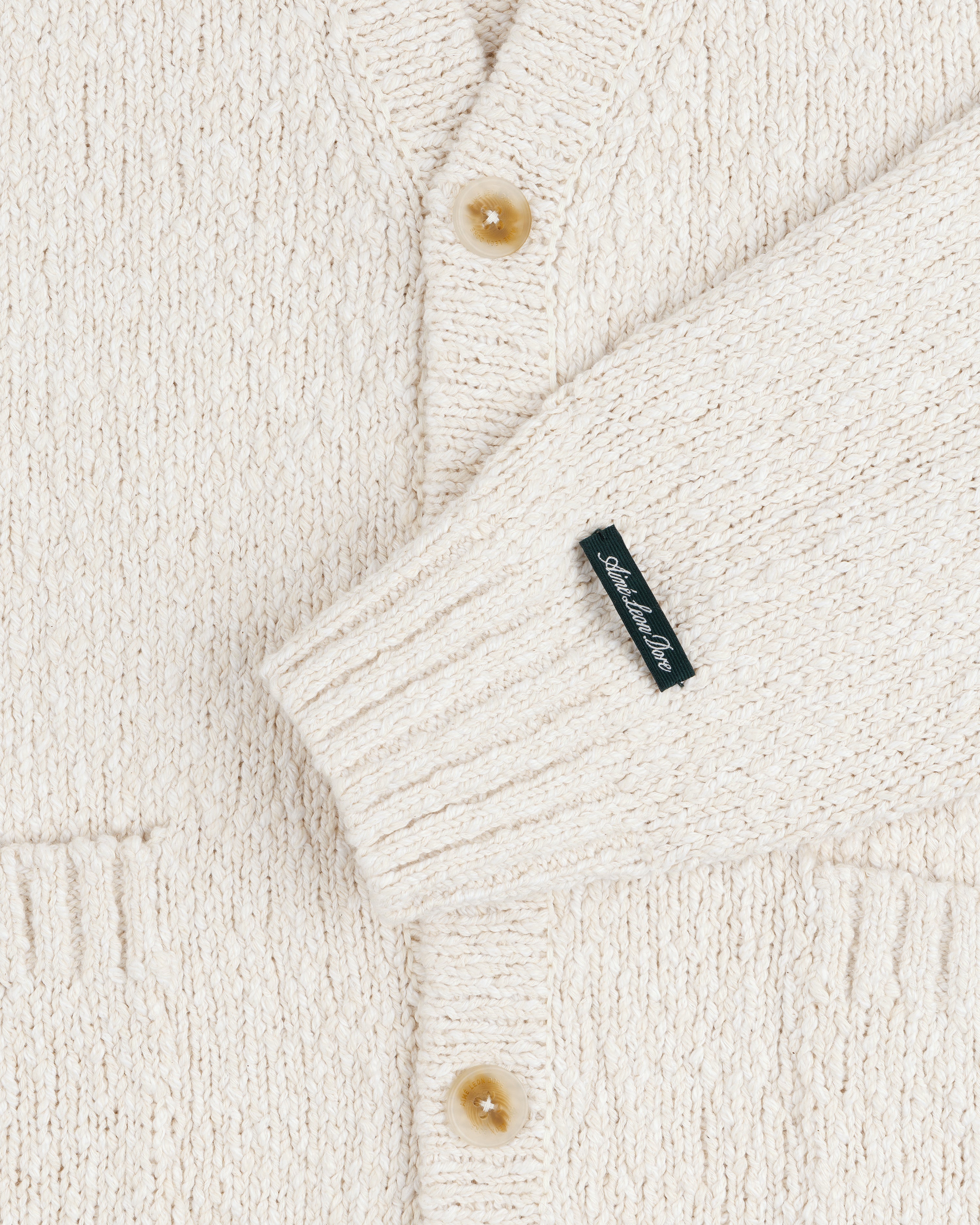 Close-up of the Cotton Slub Cardigan in cream with tan buttons and a small black sleeve label.
