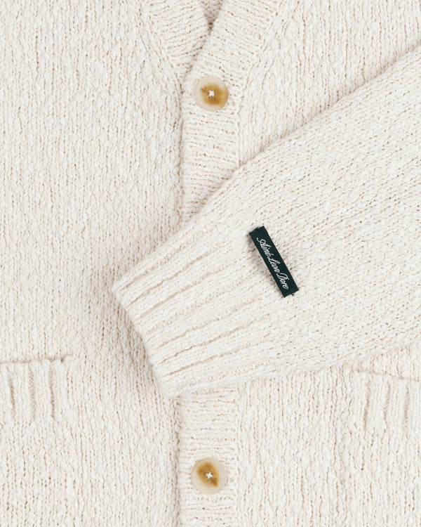 Close-up of the Cotton Slub Cardigan in cream with tan buttons and a small black sleeve label.