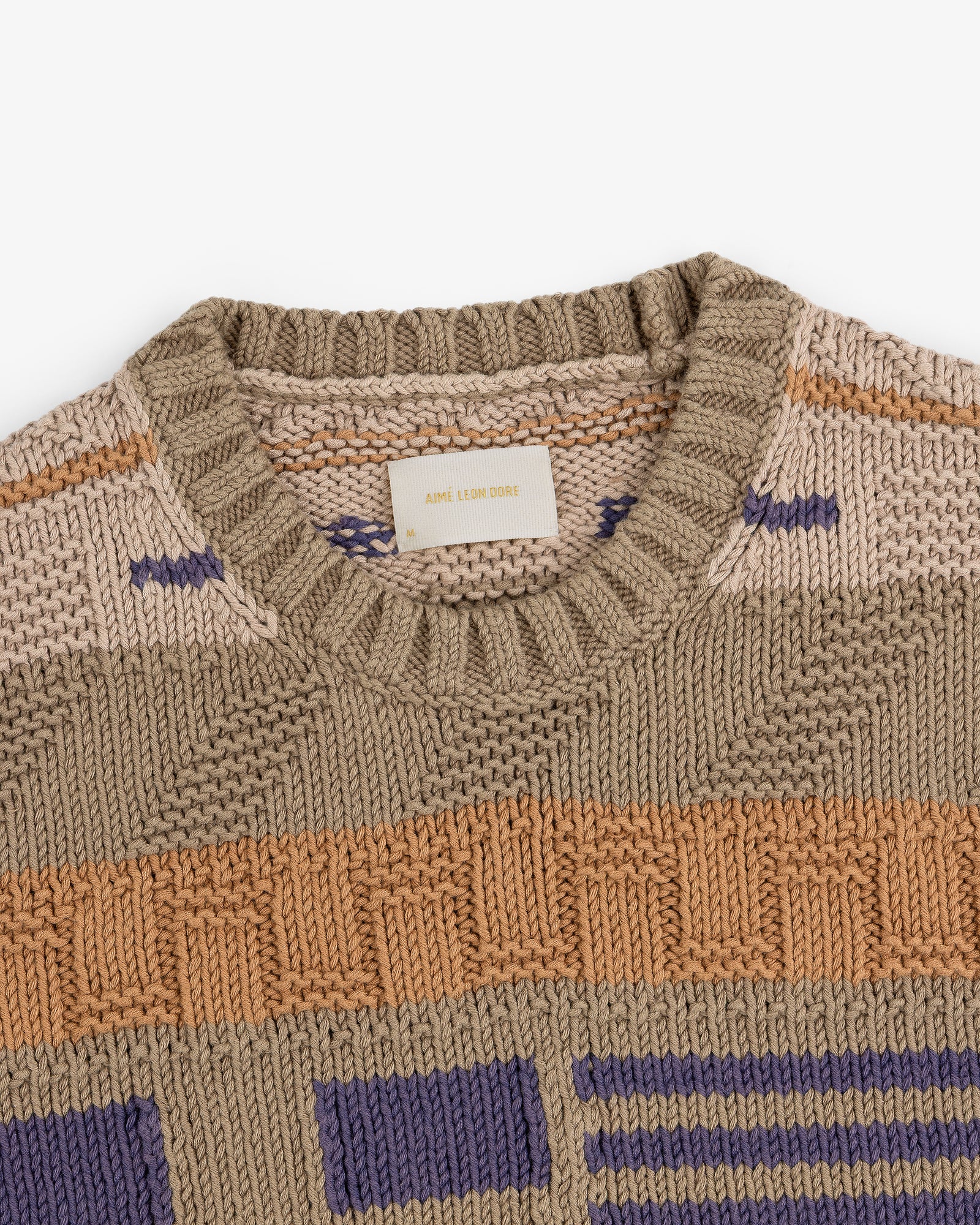 A close-up of the Simaía Crewneck Sweater with geometric patterns in beige, tan, orange, and purple.