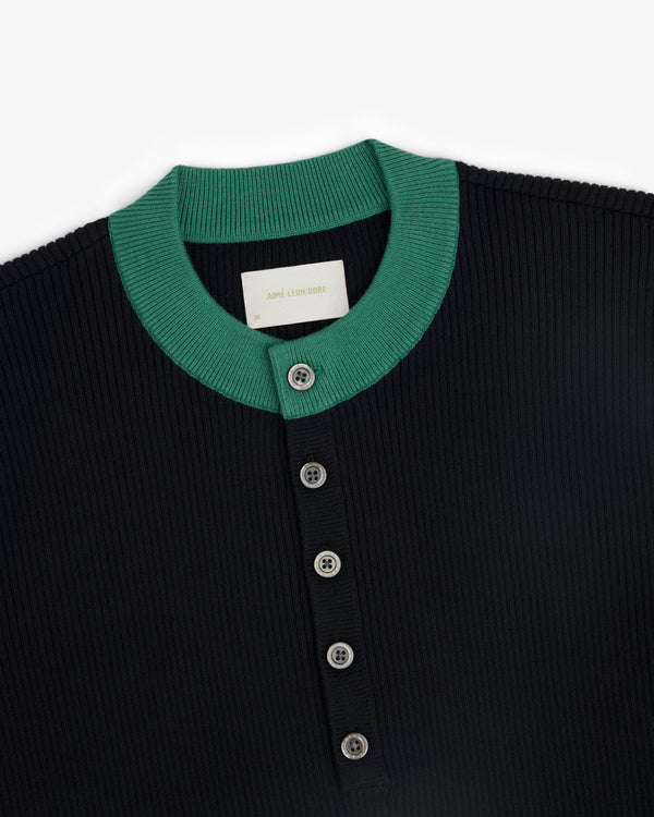 The Sport Knit Henley is a black ribbed shirt with a green collar and four buttons on the front placket.