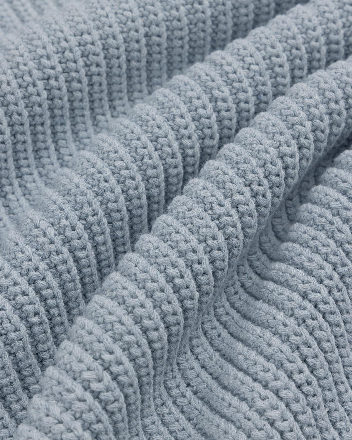 Close-up of the Knit Denim Crewneck Sweater's light blue, ribbed knit fabric with gentle textured folds.