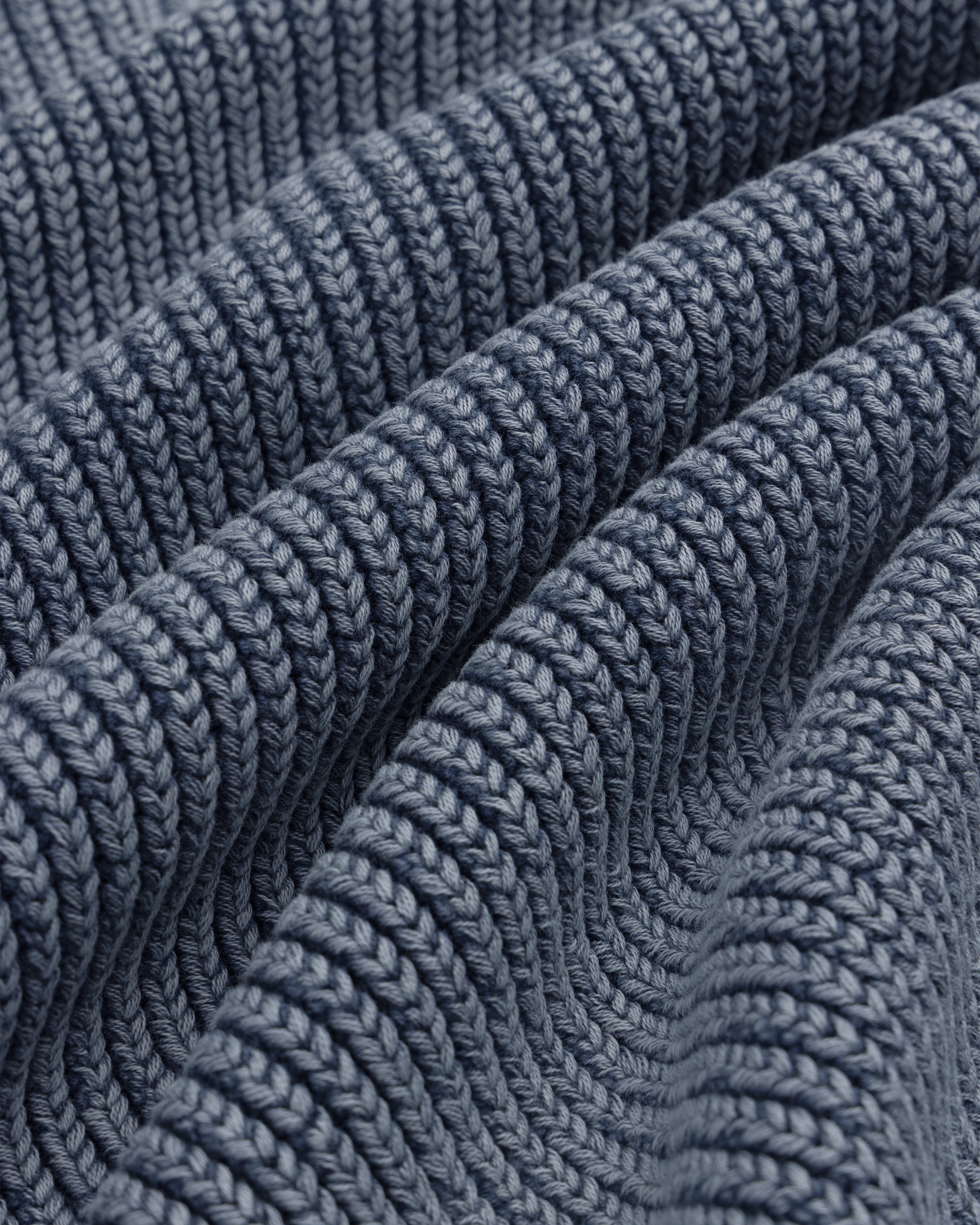 Close-up of the Stone Washed Knit Polo in blue, showing ribbed texture, wavy folds, and detailed stitching.