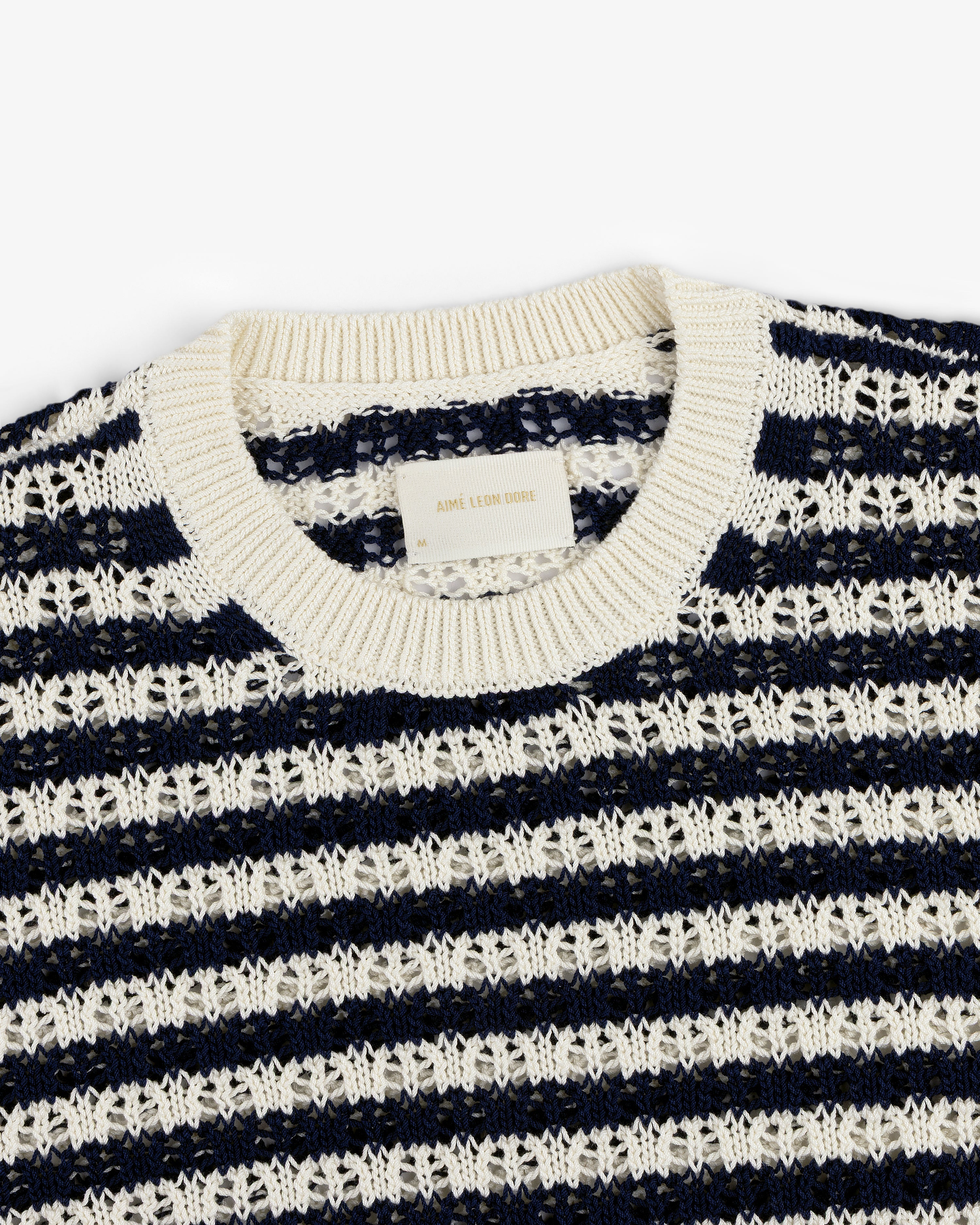 The Skáfos Sweater is navy blue with white stripes, a ribbed collar, and a visible label inside the neckline.