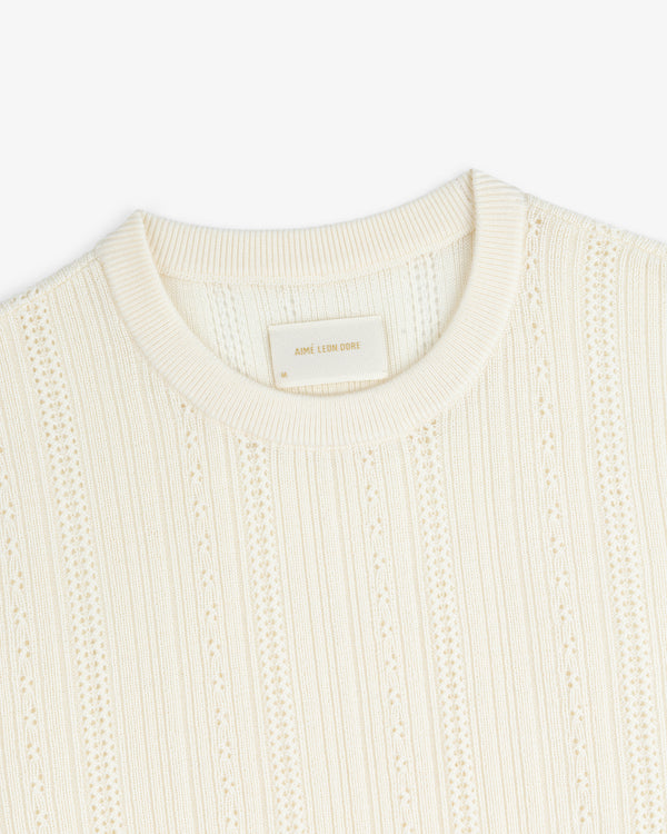 Close-up of the Merino Wool Eyelet Tee in cream, featuring textured knit, ribbed crew neck, and vertical patterns.