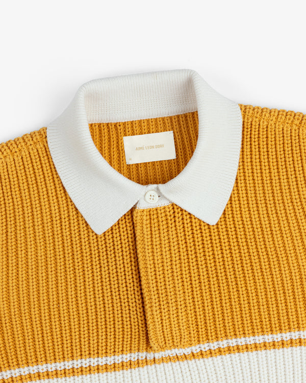 Striped Knit Rugby in mustard yellow with a white collar, button, neck label, and chest stripe.