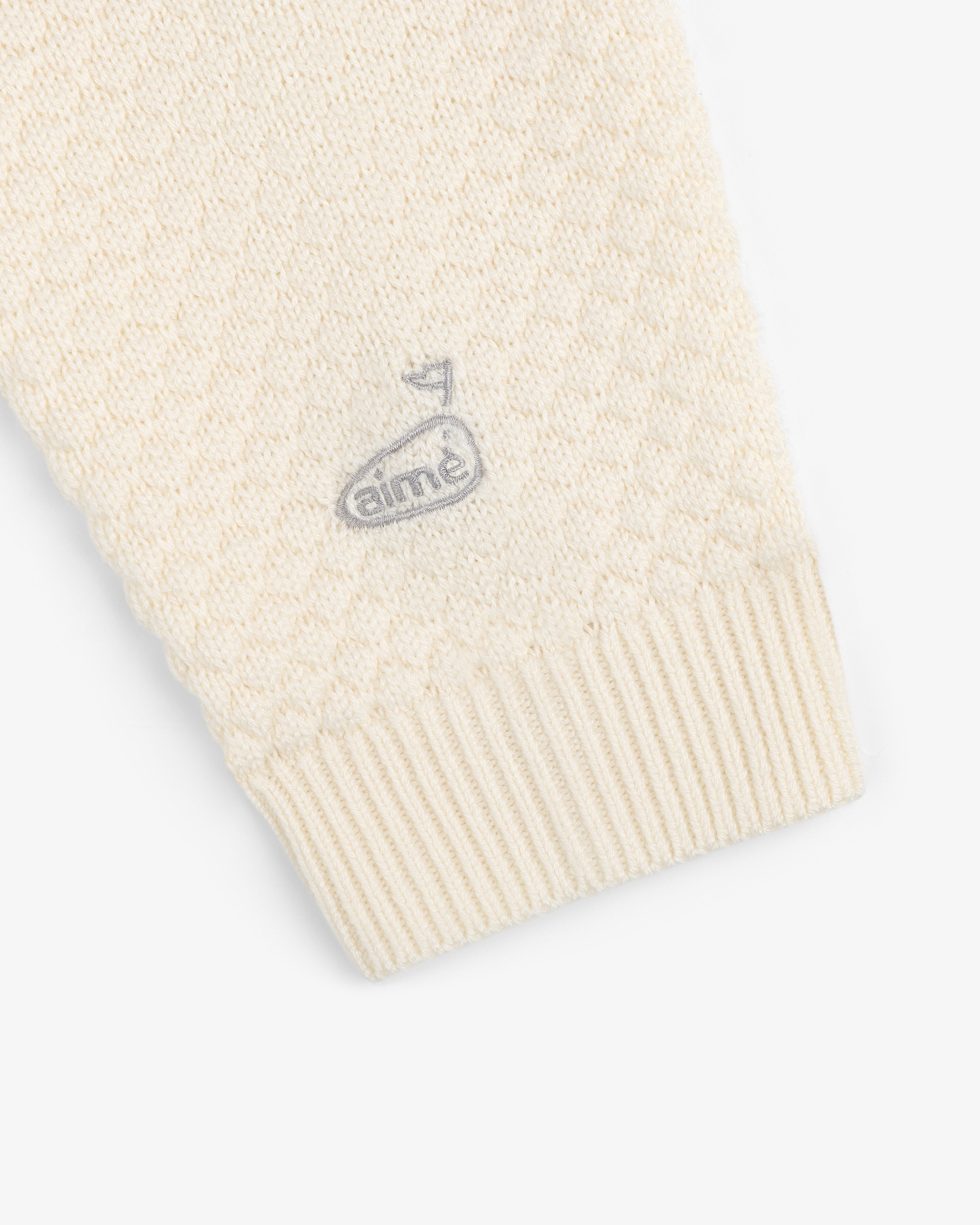 Close-up of the ALD Golf Clubhouse Sweater sleeve featuring a small embroidered logo near the cuff.