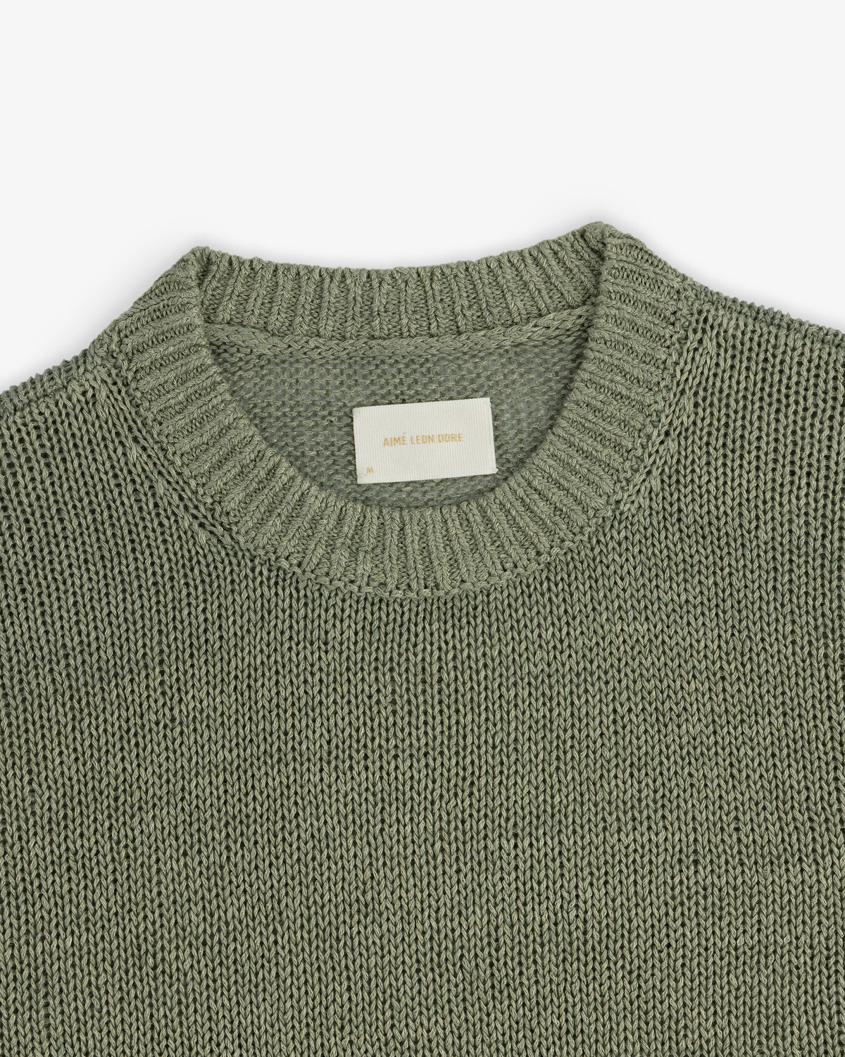 A close-up of the Linen Knit Crewneck Sweater in sage green with a ribbed neckline and inner white label.