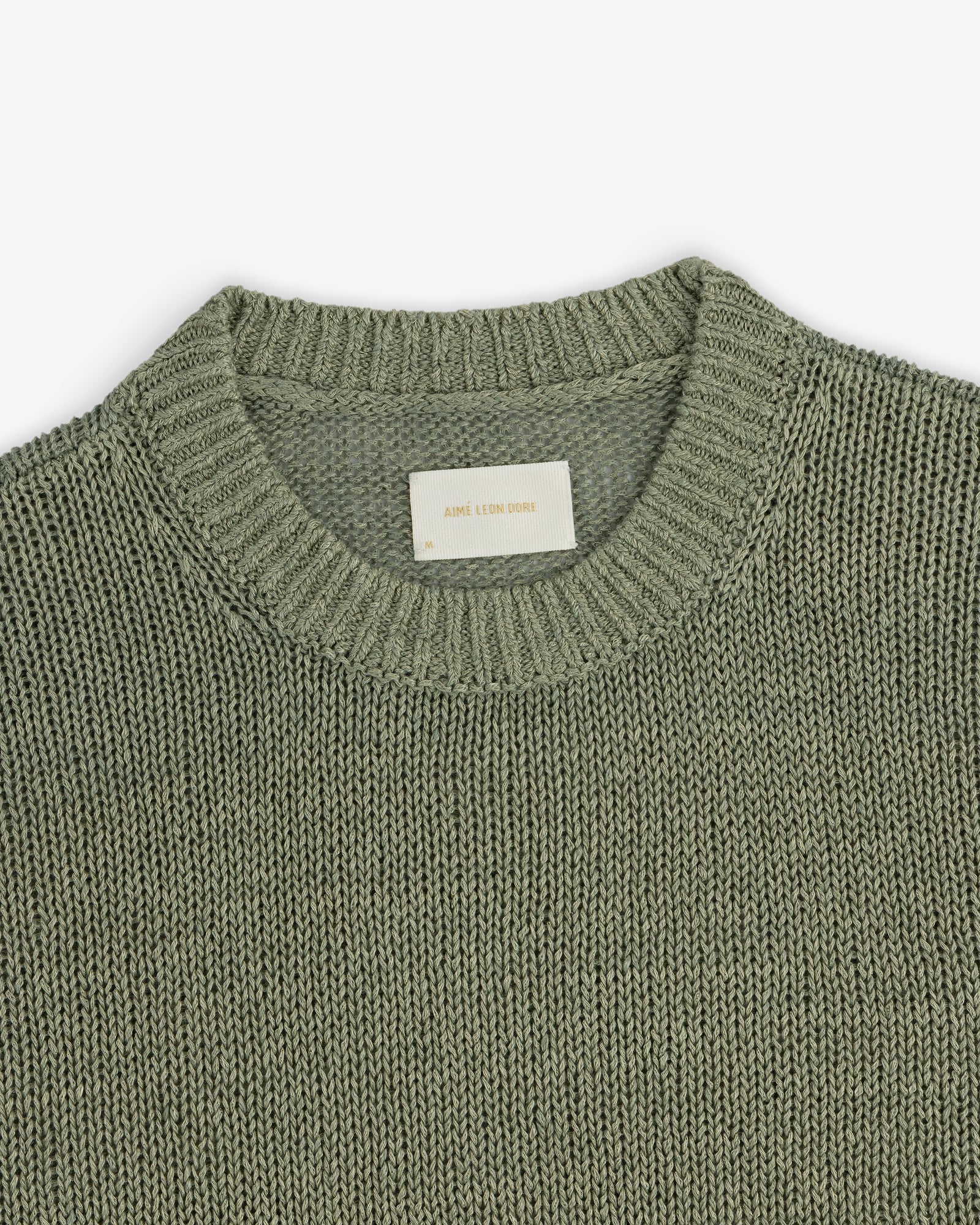 A close-up of the Linen Knit Crewneck Sweater in sage green with a ribbed neckline and inner white label.