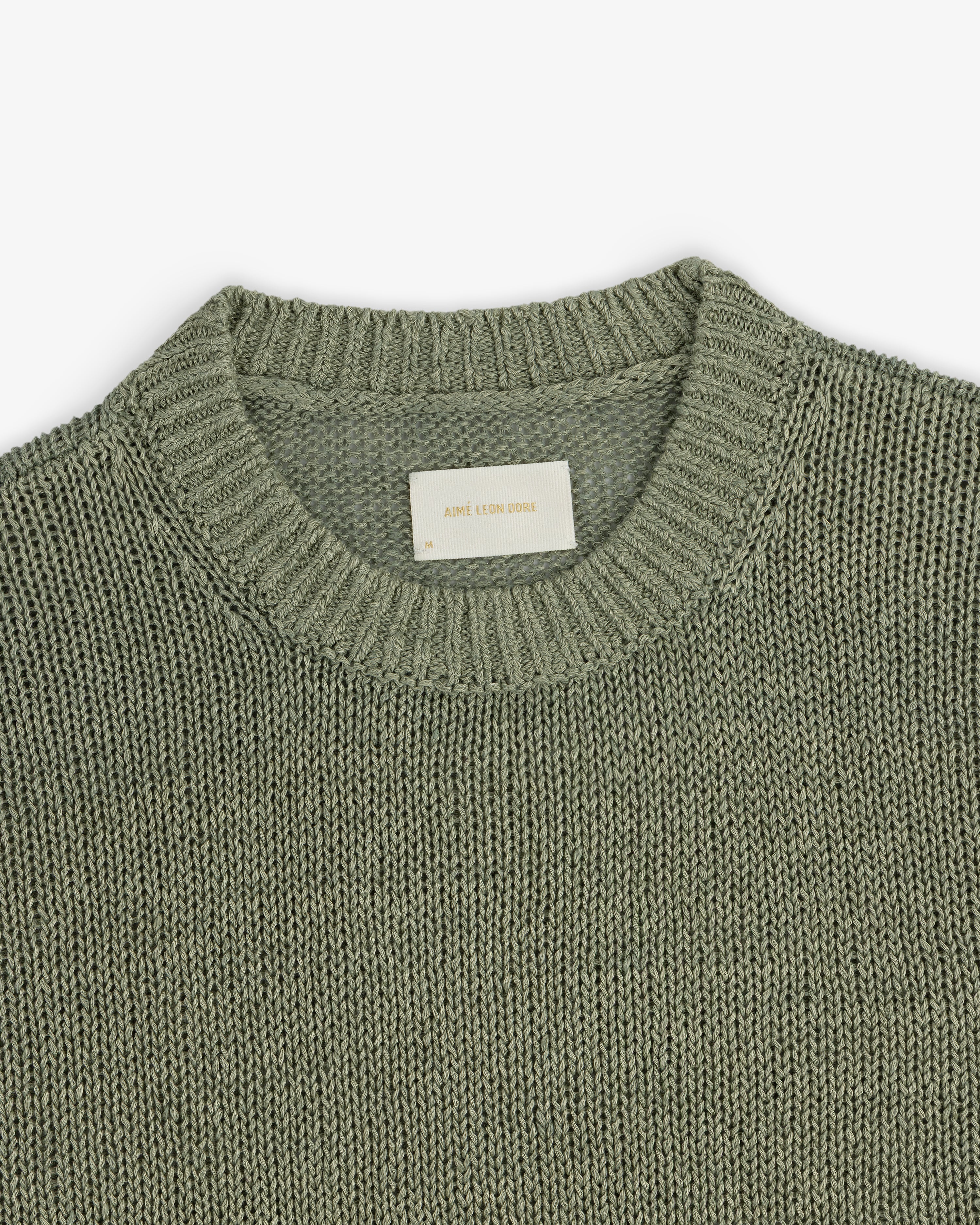 A close-up of the Linen Knit Crewneck Sweater in sage green with a ribbed neckline and inner white label.