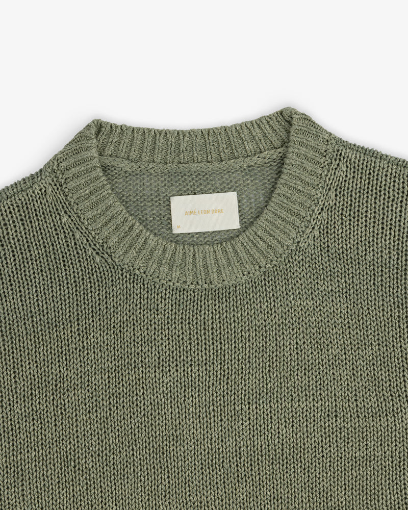 A close-up of the Linen Knit Crewneck Sweater in sage green with a ribbed neckline and inner white label.
