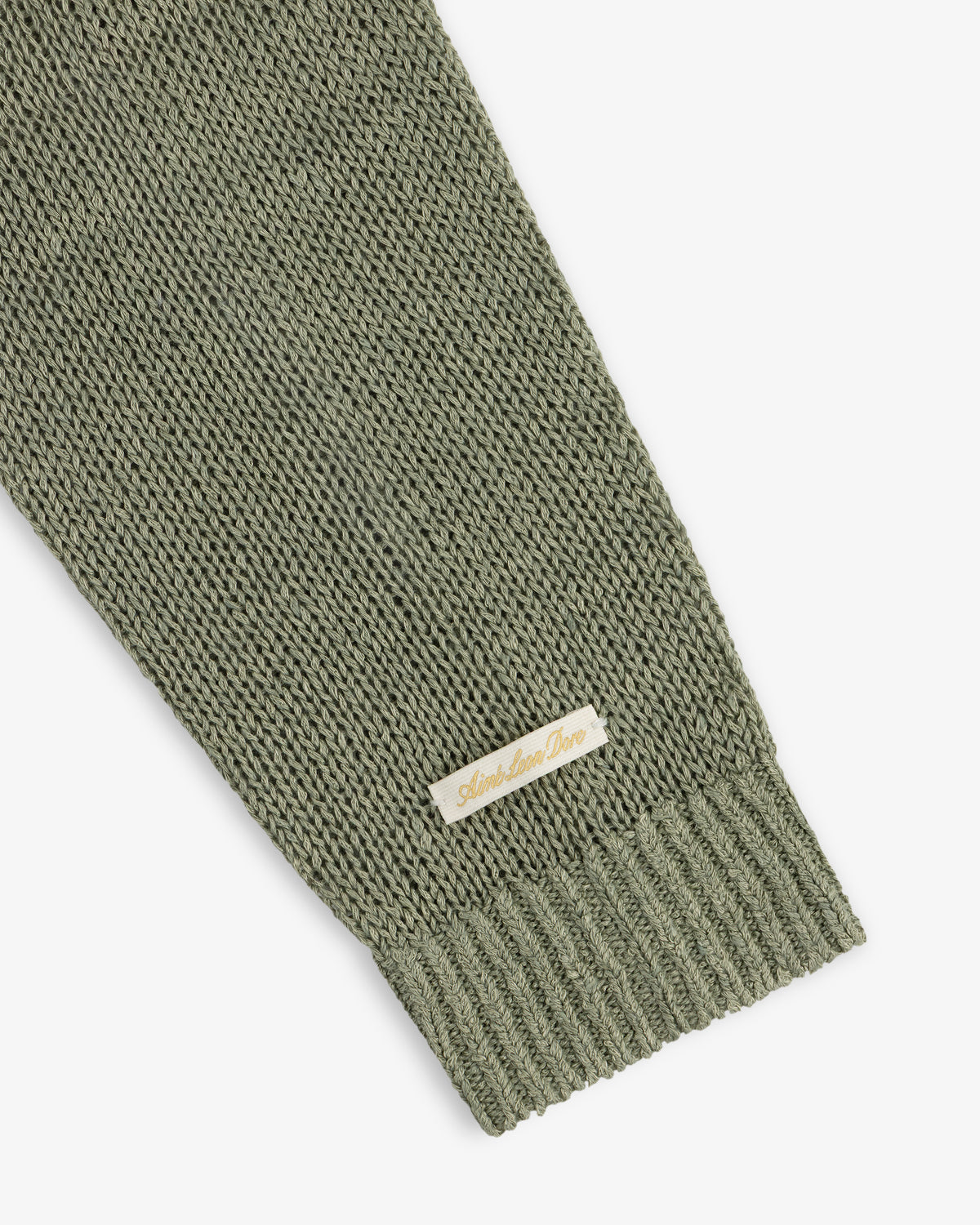 A close-up of the Linen Knit Crewneck Sweater sleeve in olive green, featuring a small beige label near the cuff.
