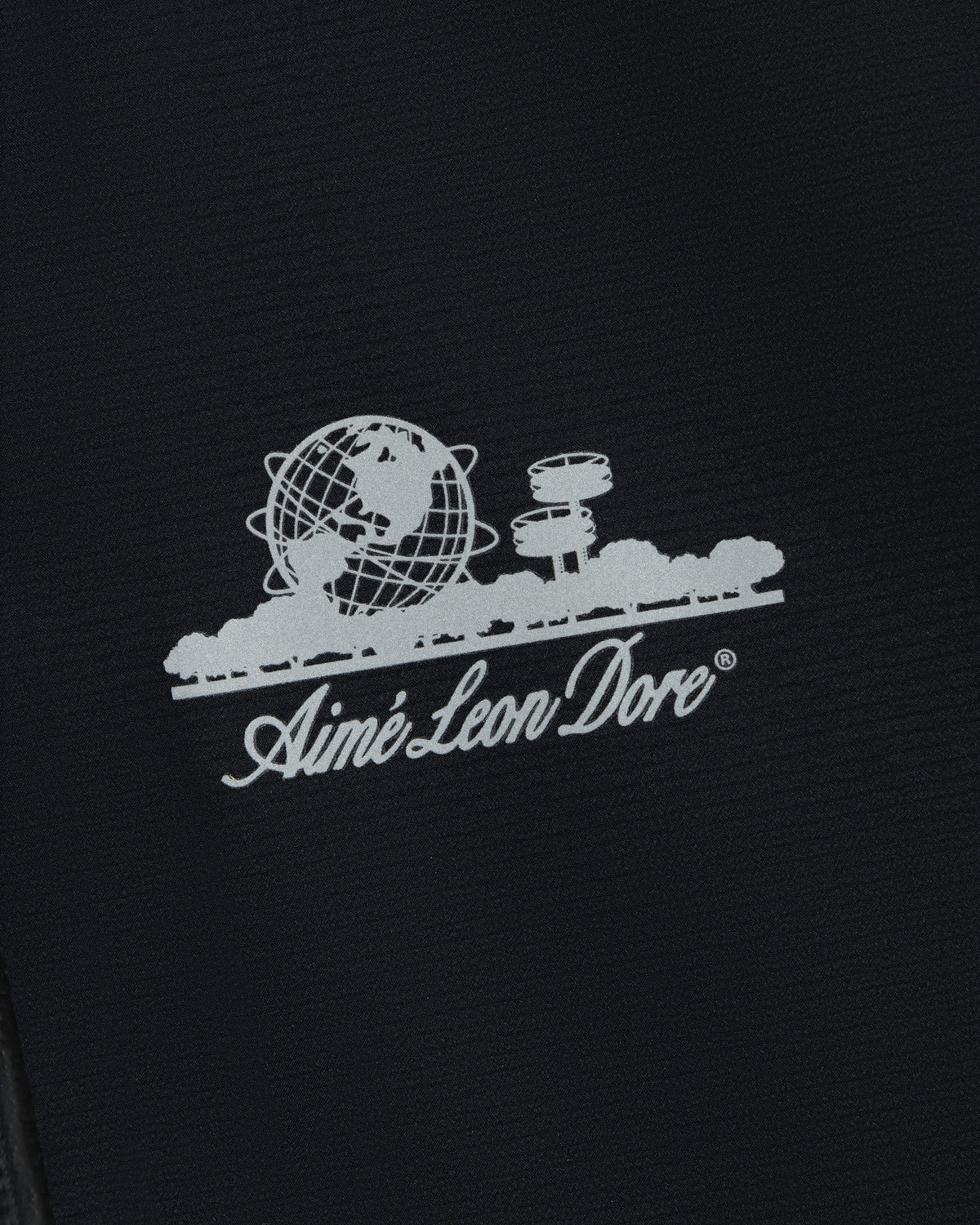 White Aimé Leon Dore logo with globe, trees, and buildings on the Lightweight GORE-TEX Shell Jacket.