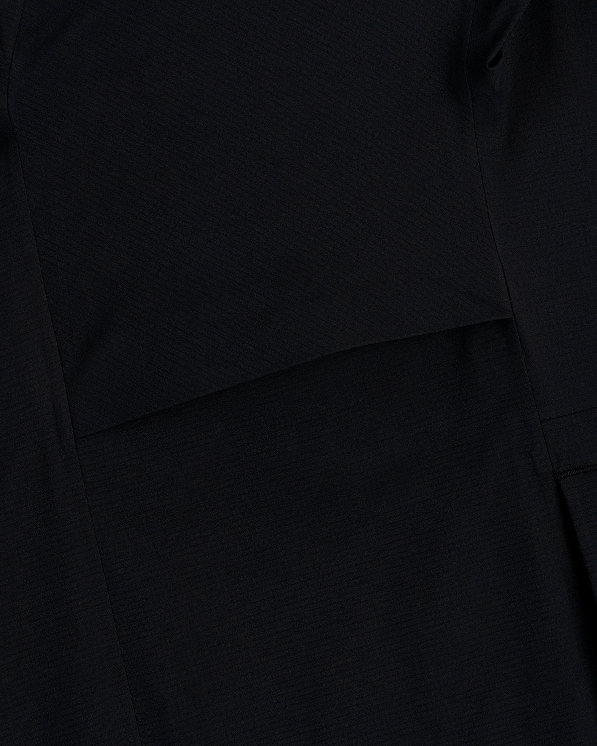 Close-up of a Lightweight GORE-TEX Shell Jacket in black, showing visible stitching and overlapping fabric layers.