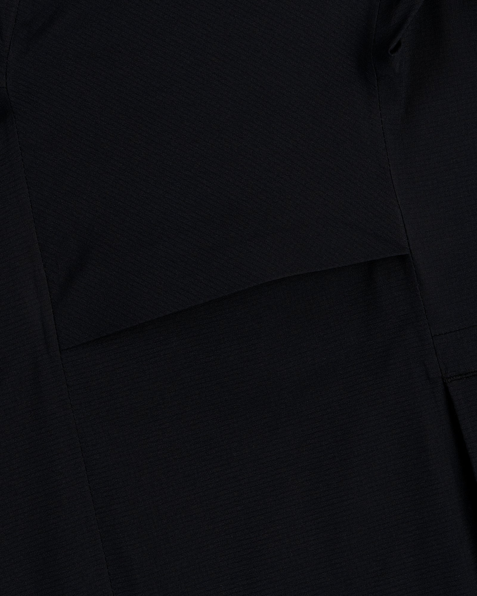 Close-up of a Lightweight GORE-TEX Shell Jacket in black, showing visible stitching and overlapping fabric layers.