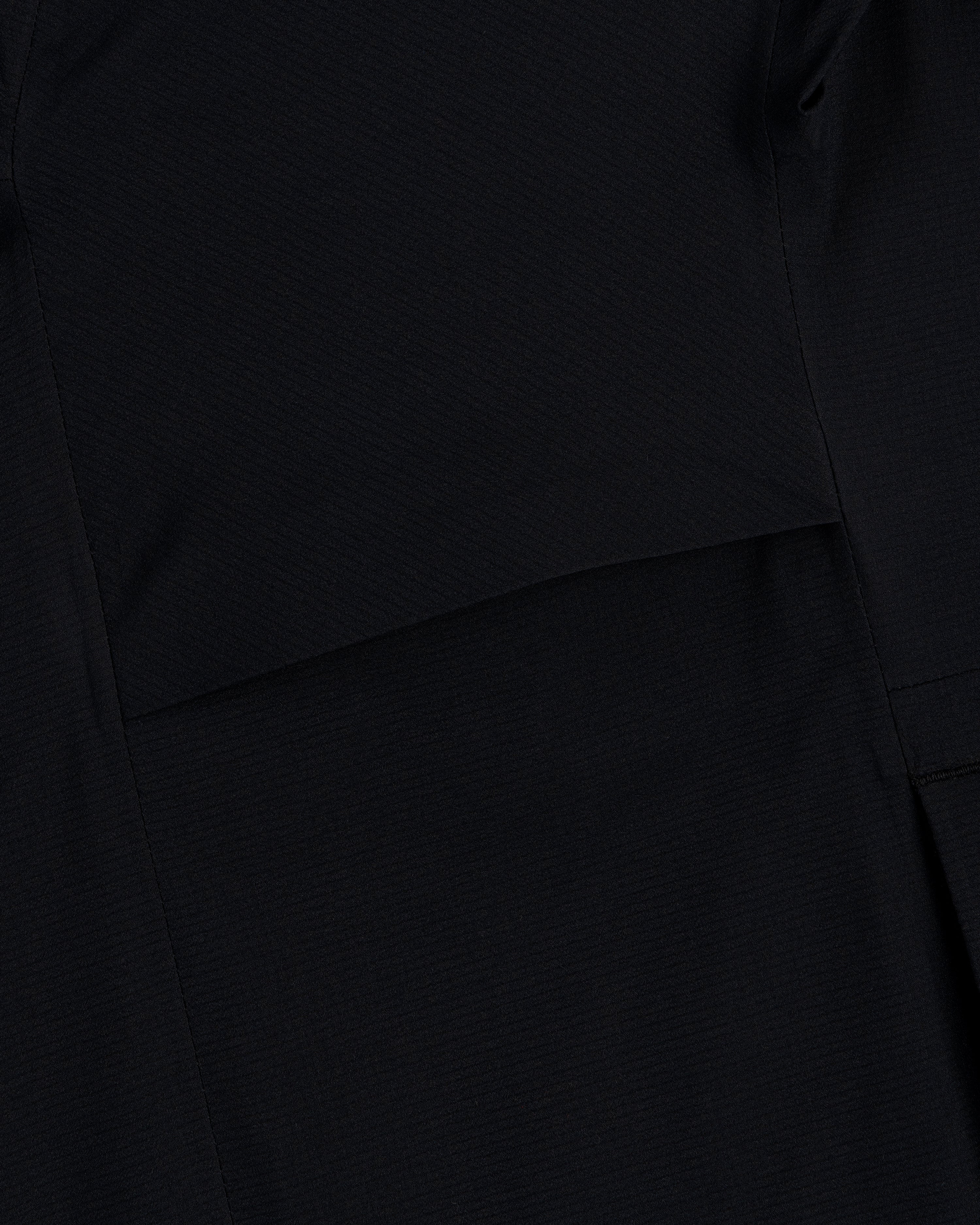 Close-up of a Lightweight GORE-TEX Shell Jacket in black, showing visible stitching and overlapping fabric layers.