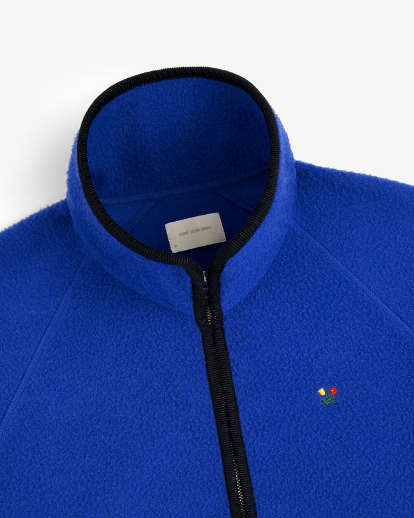 The Casentino Crest Half-Zip Pullover is bright blue with black trim and a small embroidered flower on the left chest.
