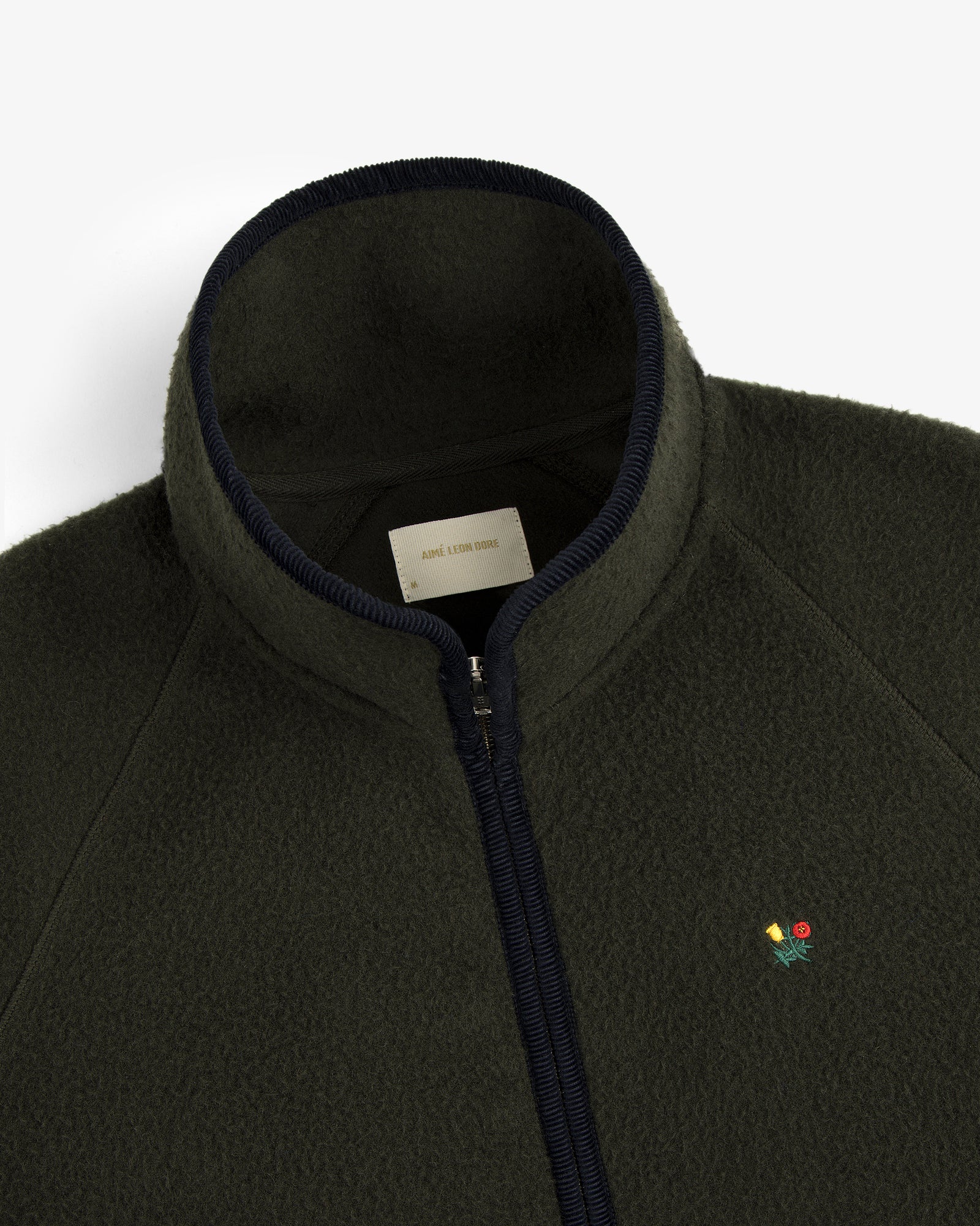 Close-up of the Casentino Crest Half-Zip Pullover, dark green with a zipper and embroidered flower logo on the chest.