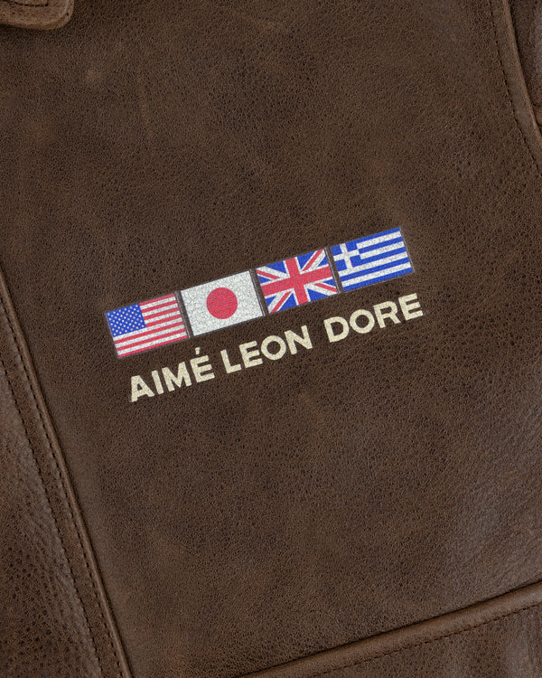 Brown leather World's Borough Leather Flight Jacket with US, Japan, UK, Greece flags above AIMÉ LEON DORE in white.