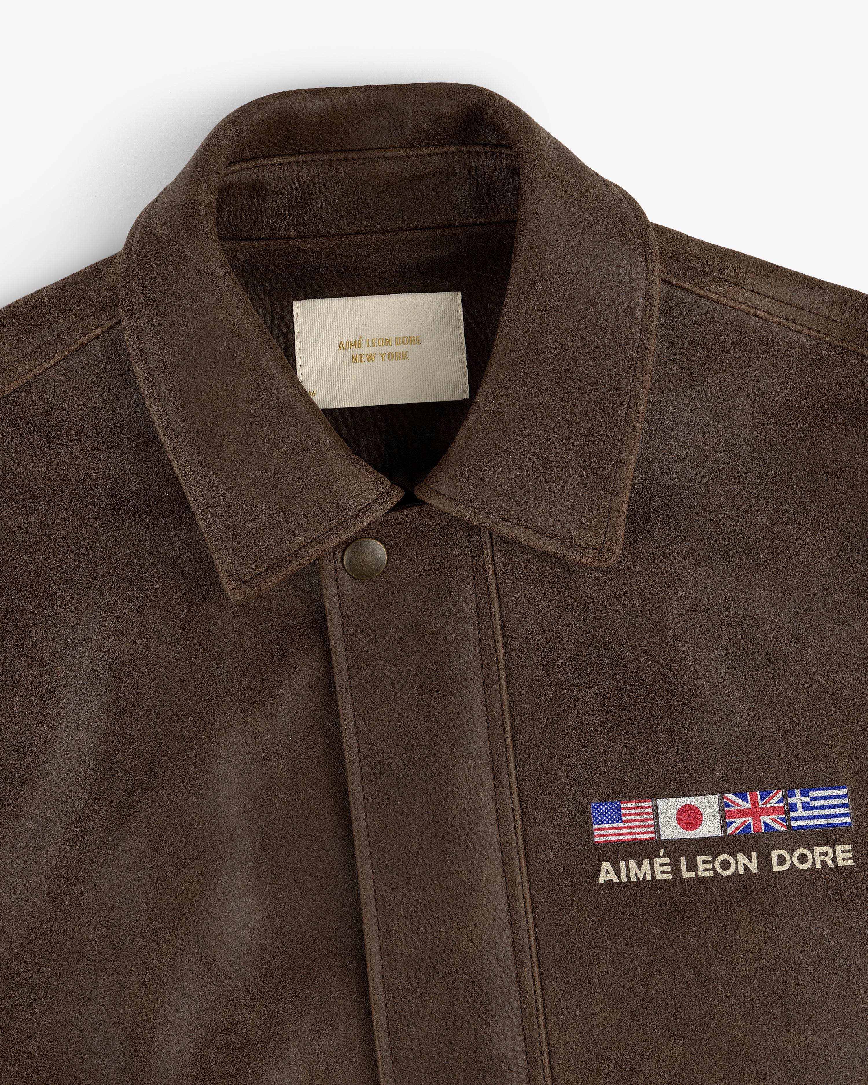 World's Borough Leather Flight Jacket in brown with collar, embroidered flags, and AIMÉ LEON DORE text above chest pocket.