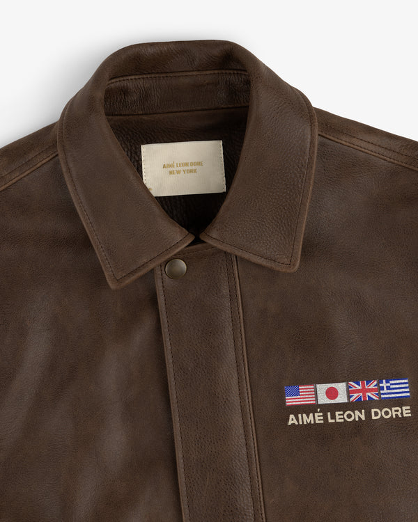 World's Borough Leather Flight Jacket in brown with collar, embroidered flags, and AIMÉ LEON DORE text above chest pocket.