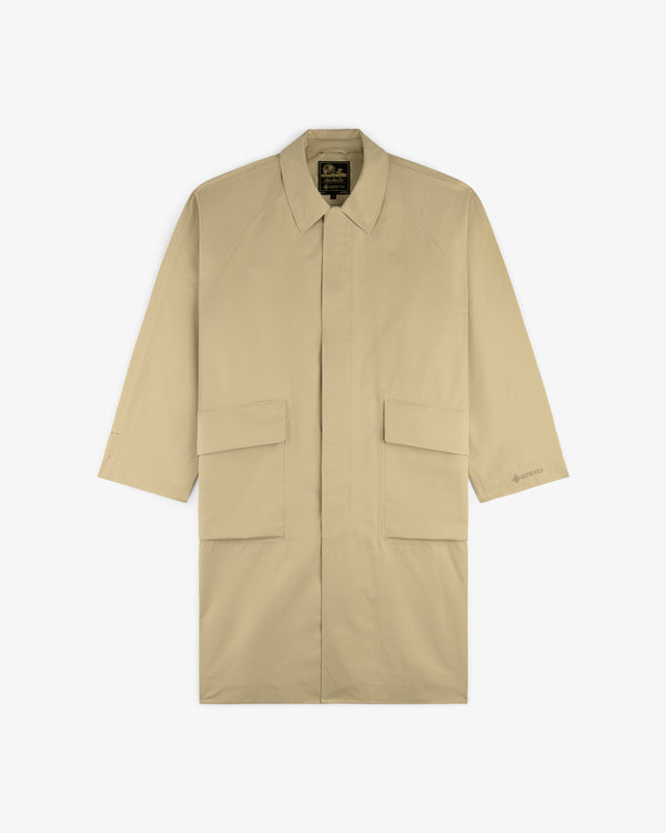 The GORE-TEX Balmacaan Coat is a beige, long-sleeve trench with large front flap pockets and a collar, laid flat.