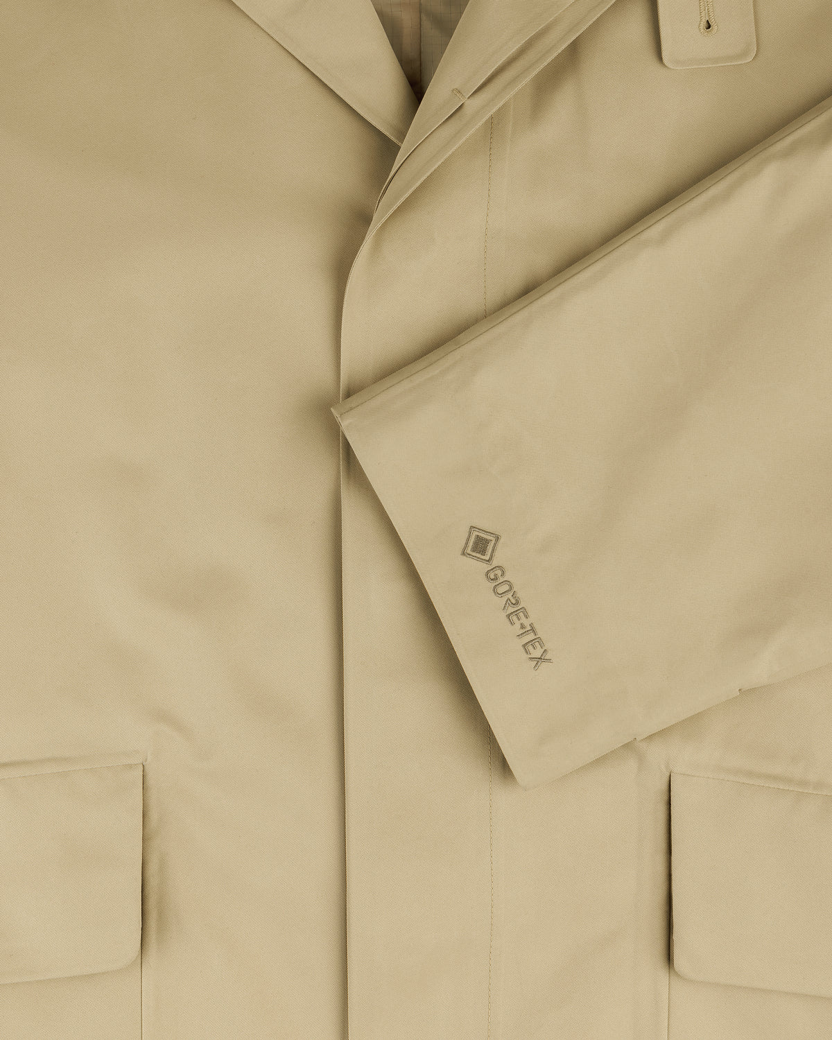 Close-up of the beige GORE-TEX Balmacaan Coat with two front pockets and a GORE-TEX logo on the sleeve.