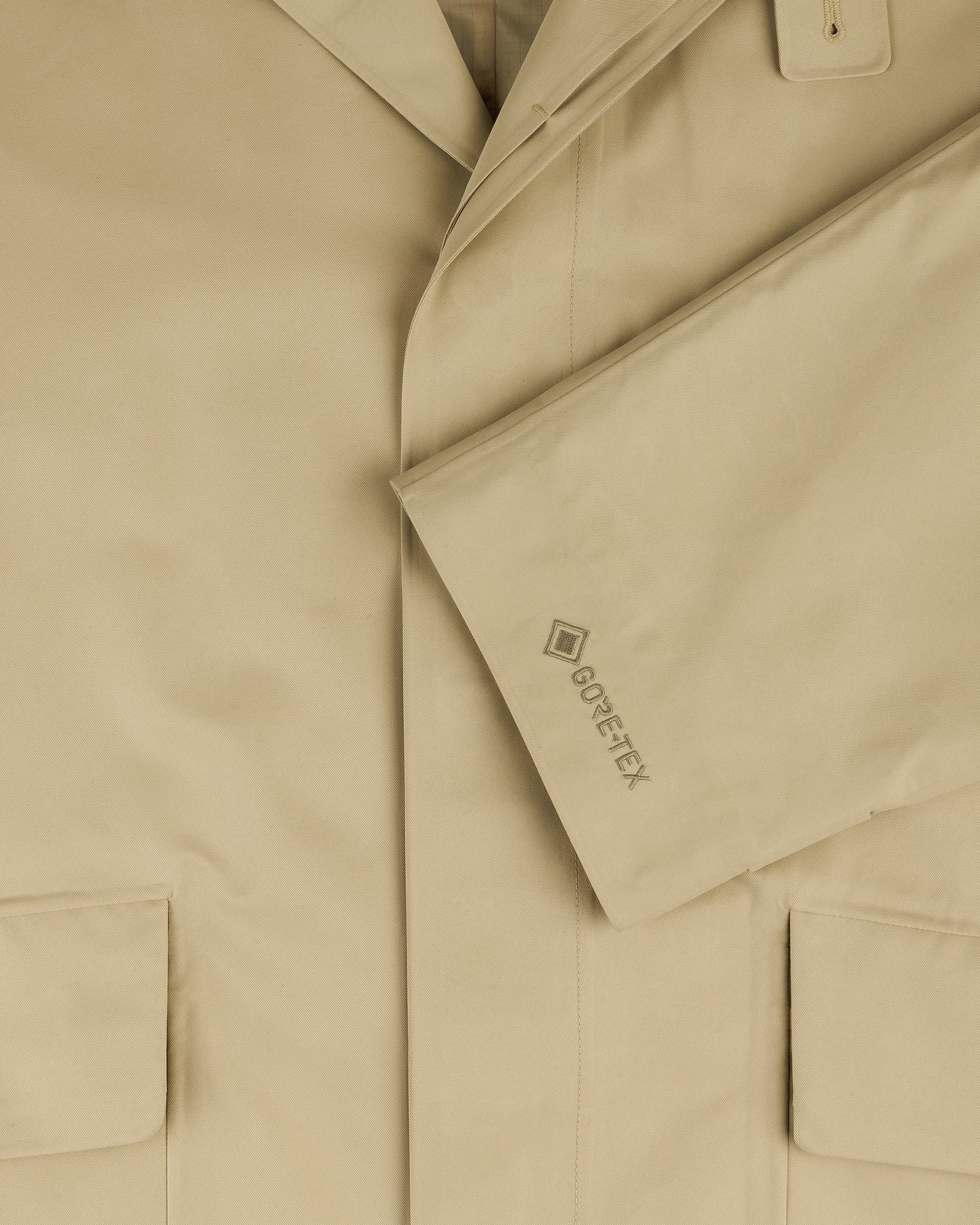 Close-up of the beige GORE-TEX Balmacaan Coat with two front pockets and a GORE-TEX logo on the sleeve.