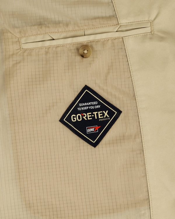 Close-up of a GORE-TEX Balmacaan Coat in beige, highlighting the GORE-TEX tag and buttoned pocket above it.