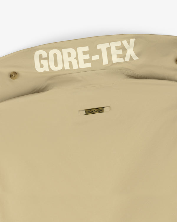 Beige GORE-TEX Balmacaan Coat with large white GORE-TEX print and a small rectangular brand label below.