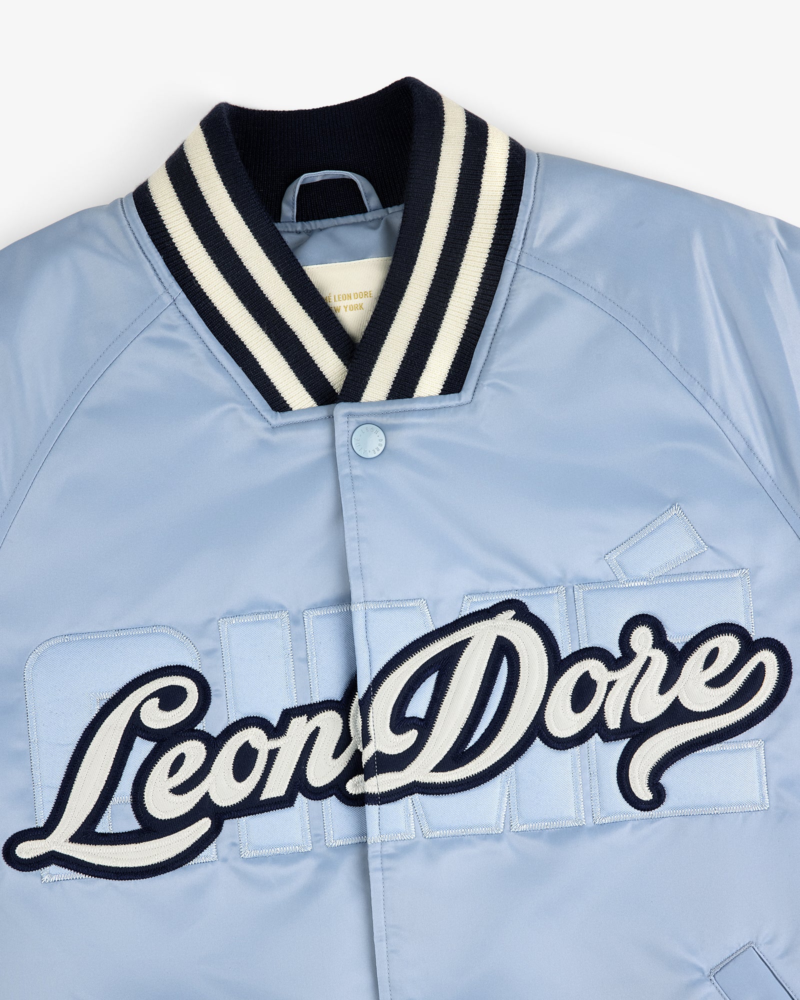 Light blue Overlay Logo Satin Varsity Jacket with striped collar and large script Leon Dore embroidery on front.