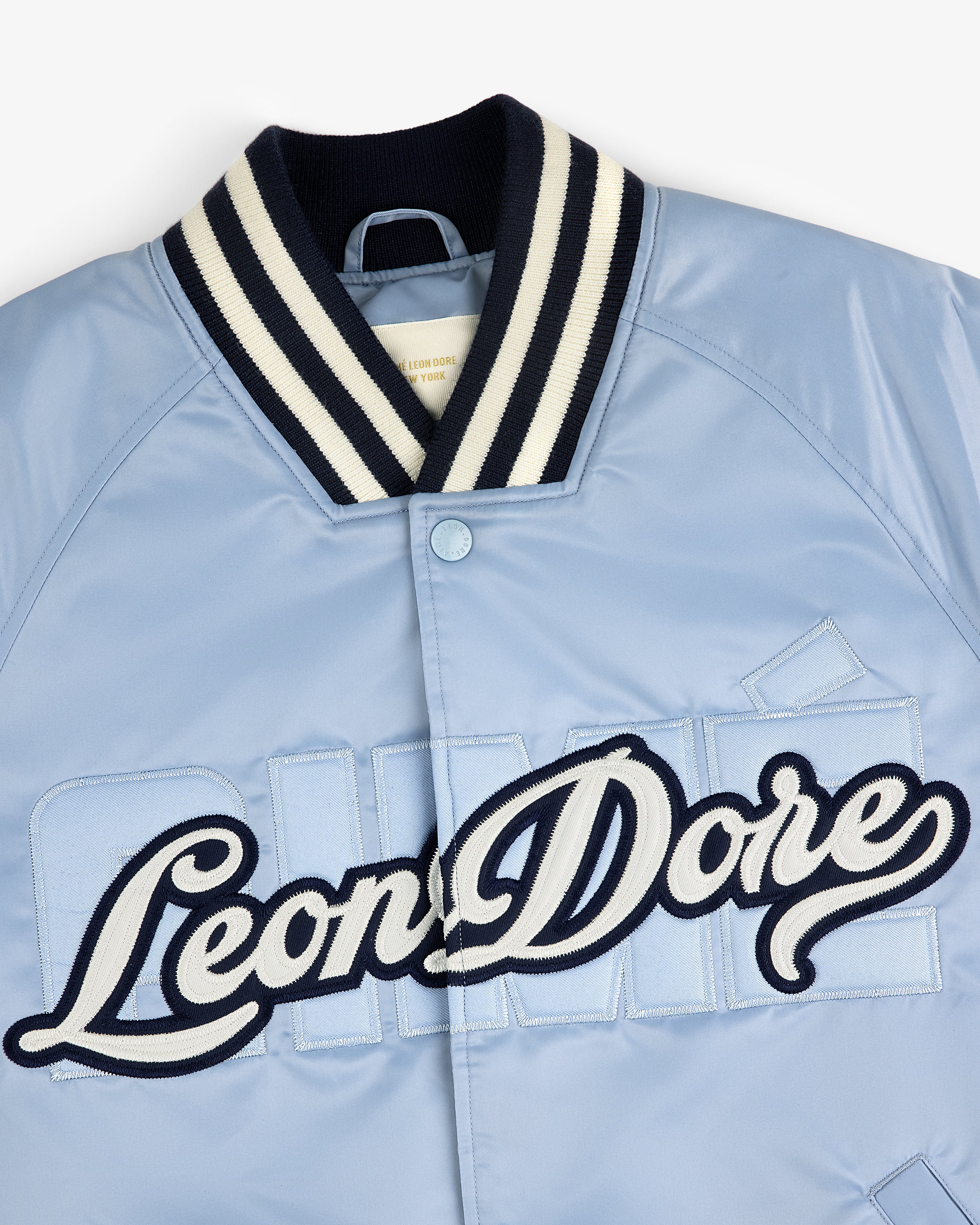 Light blue Overlay Logo Satin Varsity Jacket with striped collar and large script Leon Dore embroidery on front.