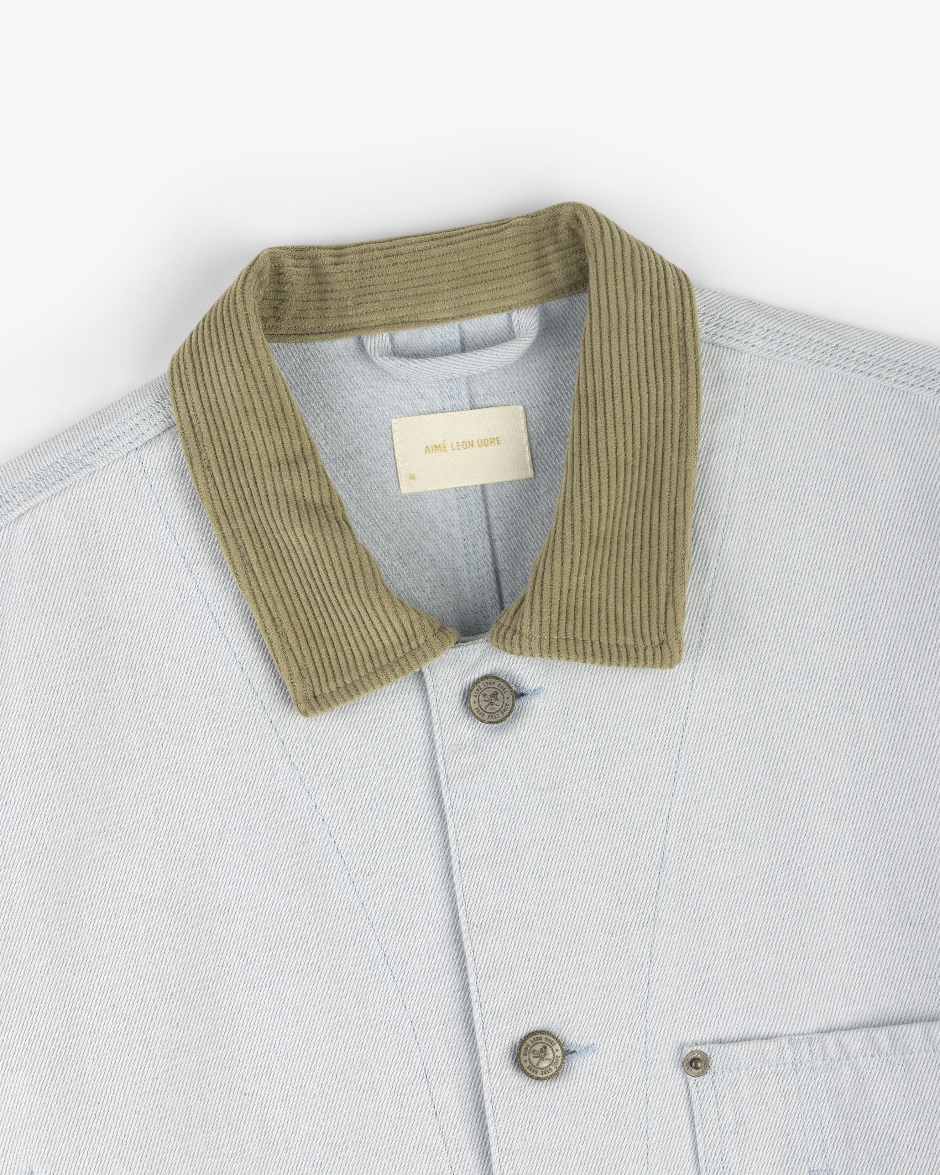 Denim Barn Jacket in light blue with ribbed olive green collar, visible buttons, and a chest pocket.