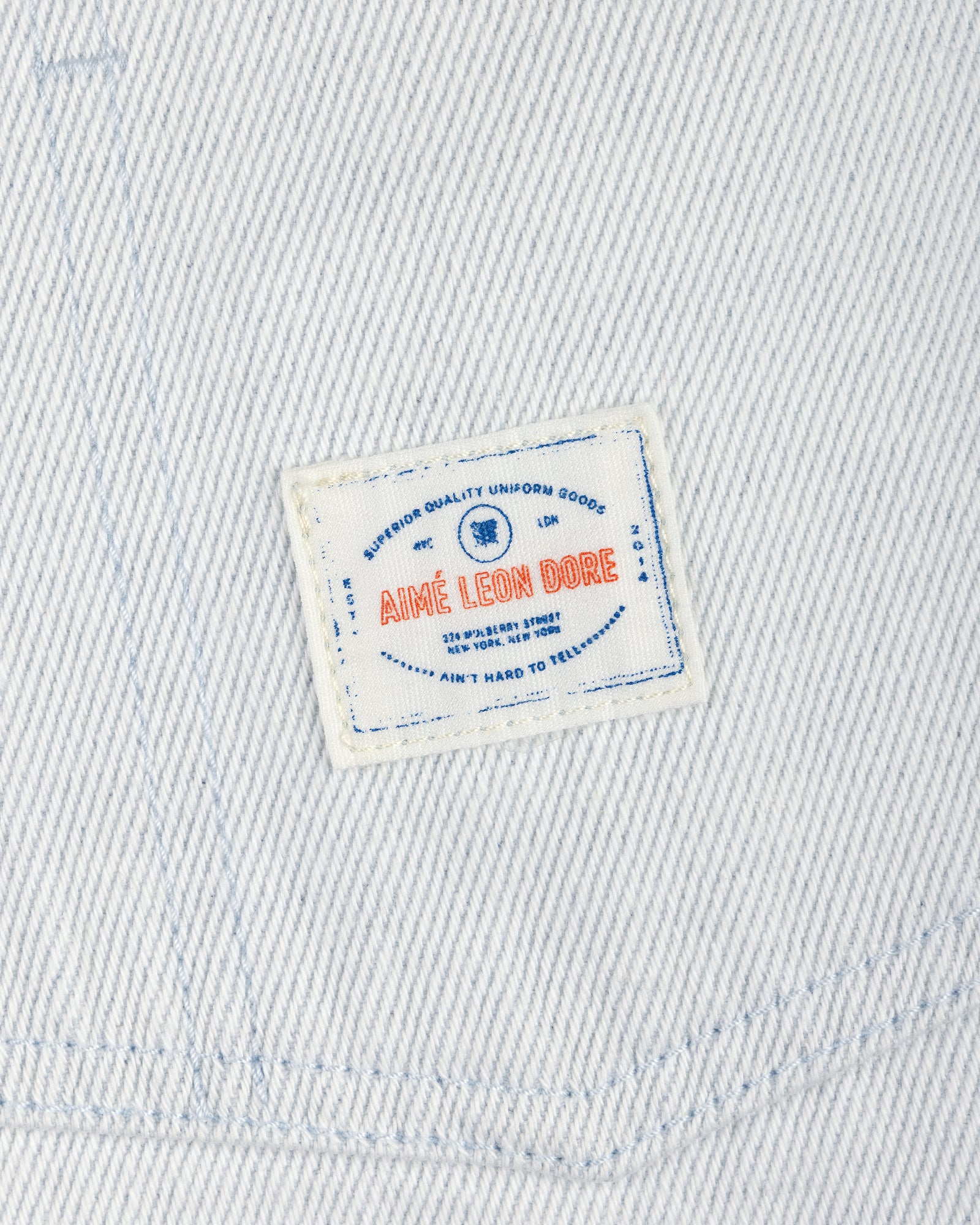The Denim Barn Jacket features white denim and a rectangular patch label with AIMÉ LEON DORE in red and blue text.