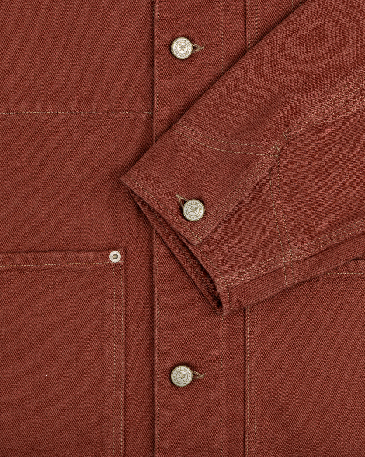 Close-up of the Denim Barn Jacket in rust, highlighting metal buttons, stitching, pocket, and sleeve.