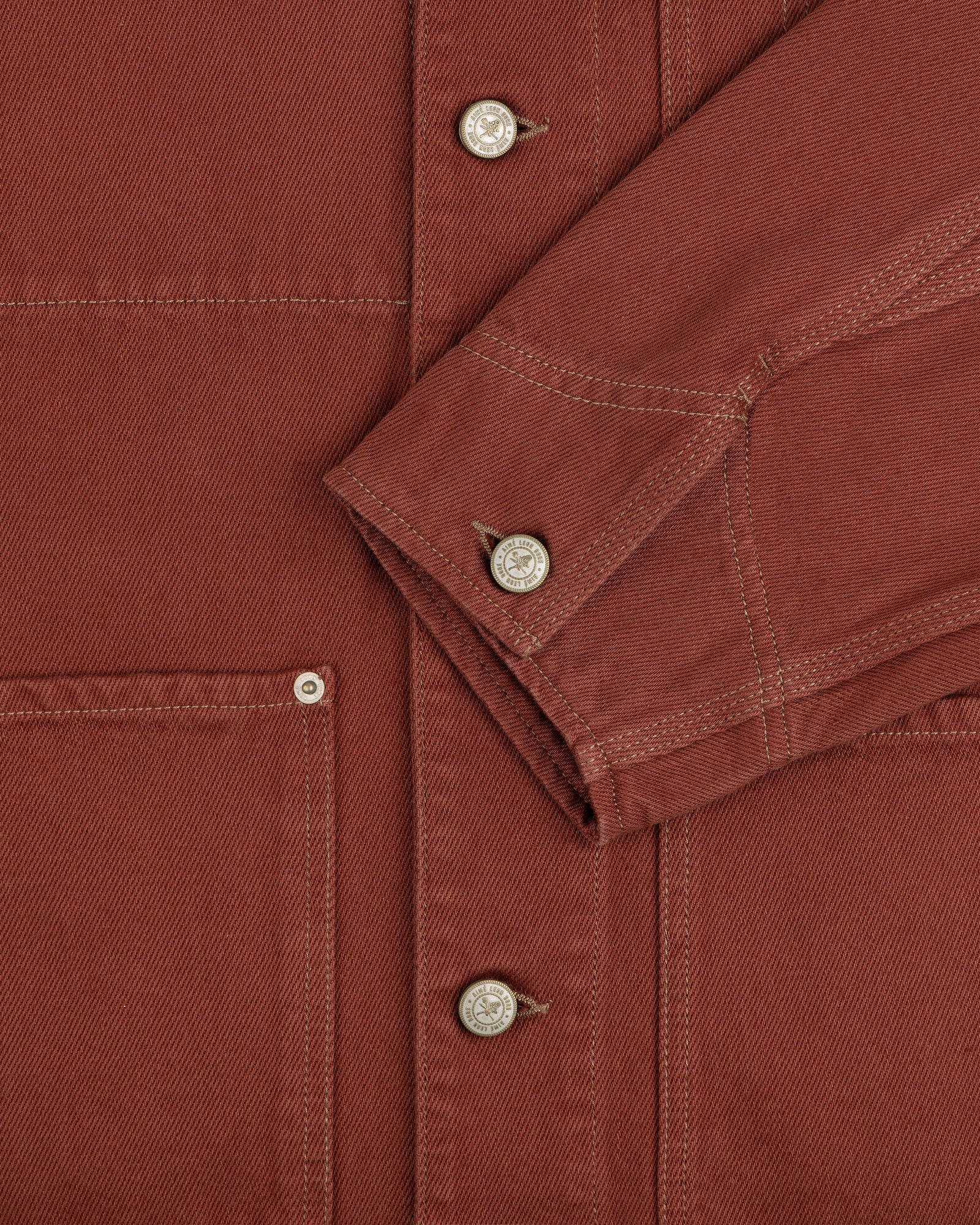 Close-up of the Denim Barn Jacket in rust, highlighting metal buttons, stitching, pocket, and sleeve.