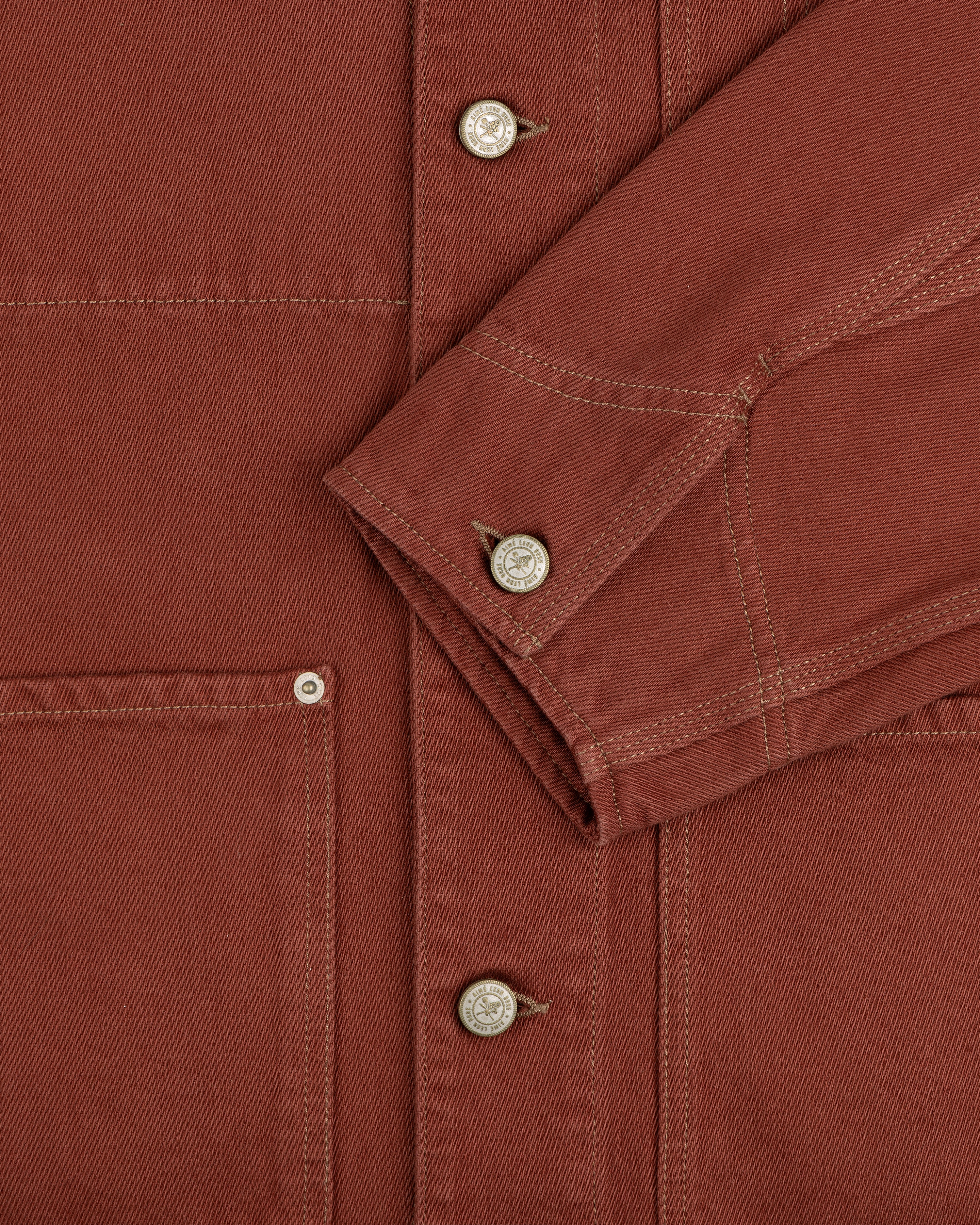 Close-up of the Denim Barn Jacket in rust, highlighting metal buttons, stitching, pocket, and sleeve.
