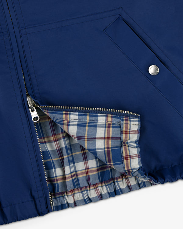 Close-up of the Reversible Madras Windbreaker, featuring a blue shell, silver zipper, and plaid cream, blue & red lining.