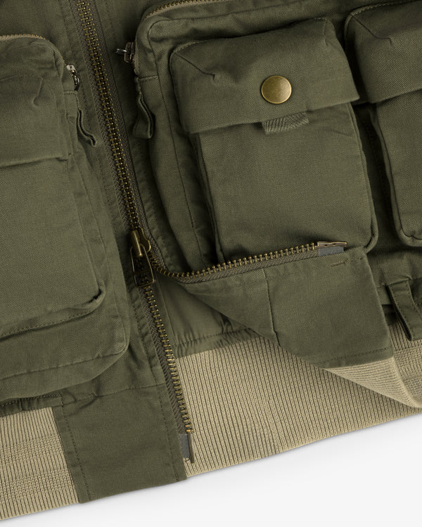 Close-up of the Safari Utility Bomber in olive green with multiple pockets, zippers, and a snap button pocket.