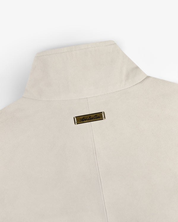 Suede Track Jacket in beige with a tall collar and small gold nameplate on the back near the neckline.