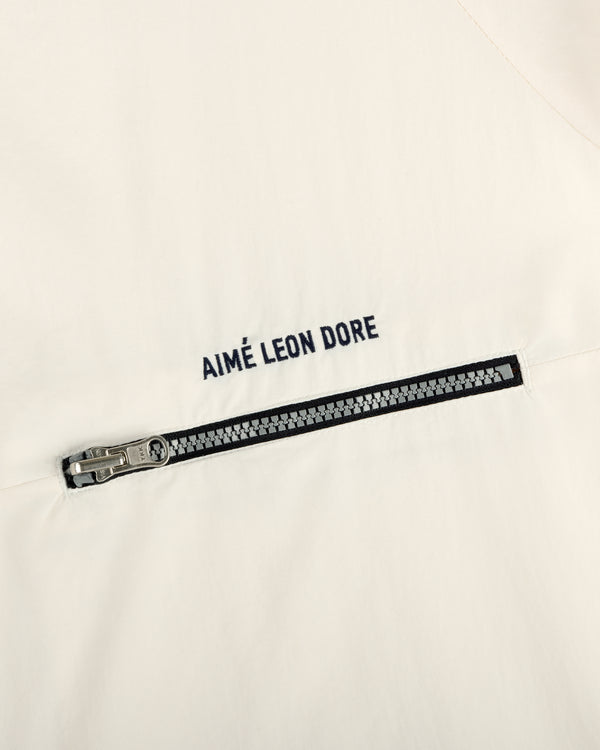 Close-up of an off-white Nylon Packable Windbreaker with a black zipper and AIMÉ LEON DORE text above the zipper.