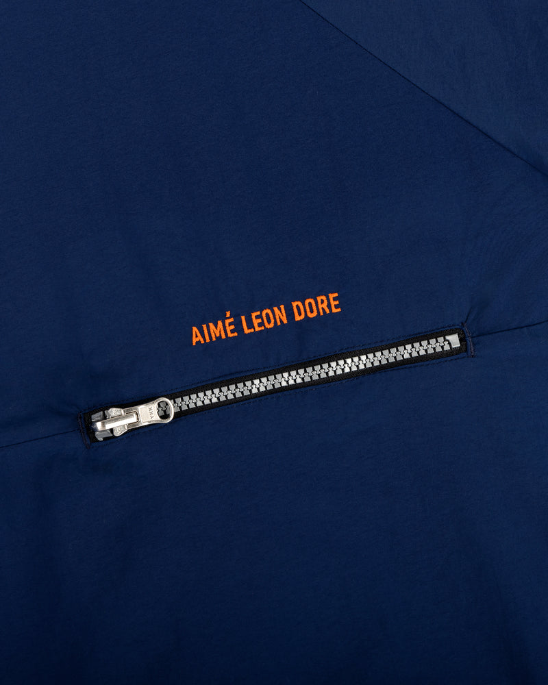 Close-up of a navy Nylon Packable Windbreaker with a silver zipper and Aimé Leon Dore in orange above the zipper.
