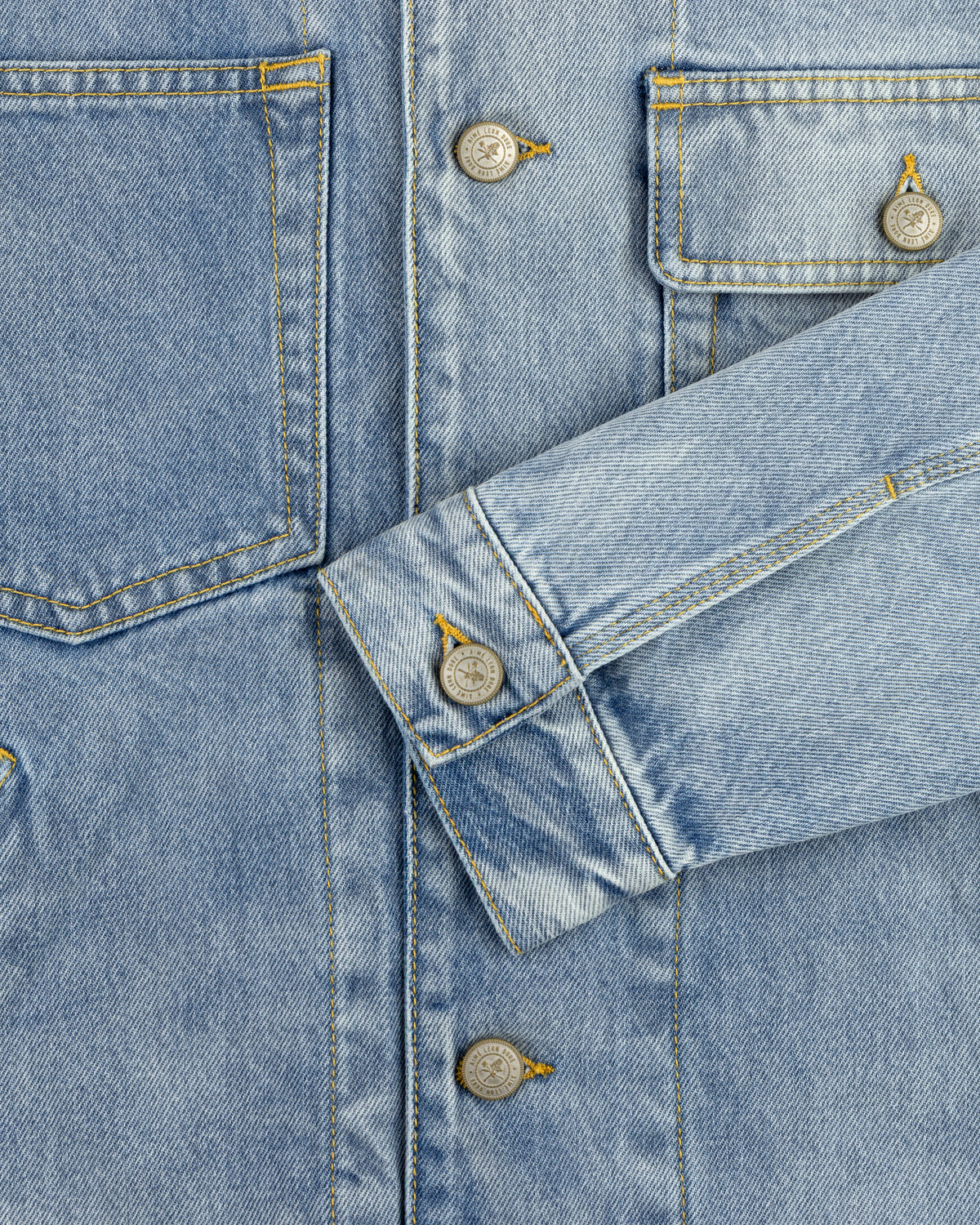 Close-up of a Denim Trucker Jacket highlighting pockets, buttons, and an overlapped sleeve in blue denim.