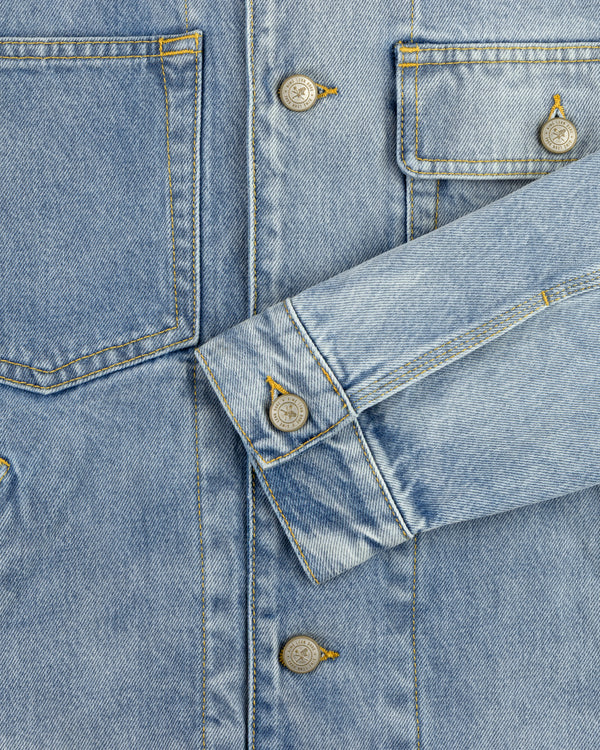 Close-up of a Denim Trucker Jacket highlighting pockets, buttons, and an overlapped sleeve in blue denim.