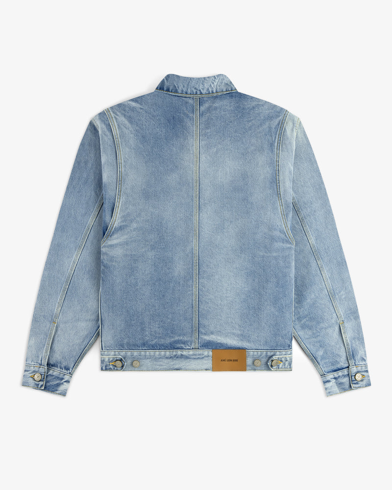 The Denim Trucker Jacket is light blue with a tan leather patch near the bottom hem on the back.