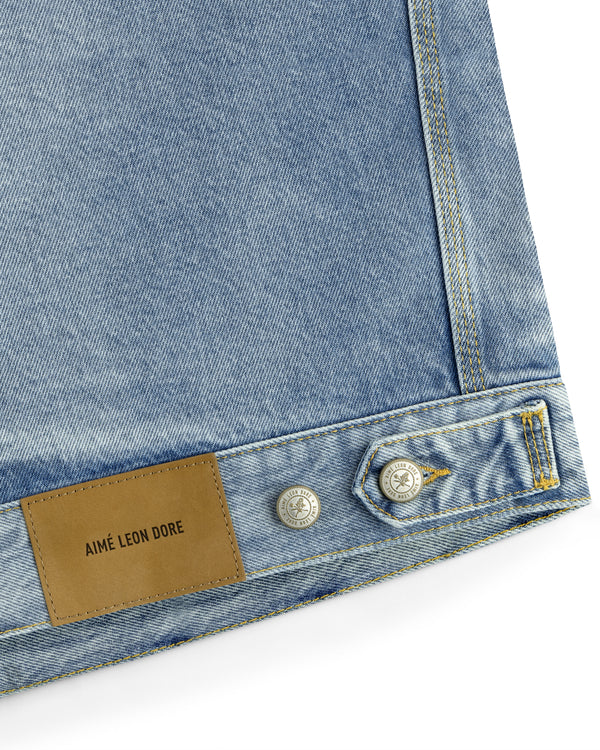 Light blue Denim Trucker Jacket with silver buttons and a brown leather AIMÉ LEON DORE patch on the bottom edge.