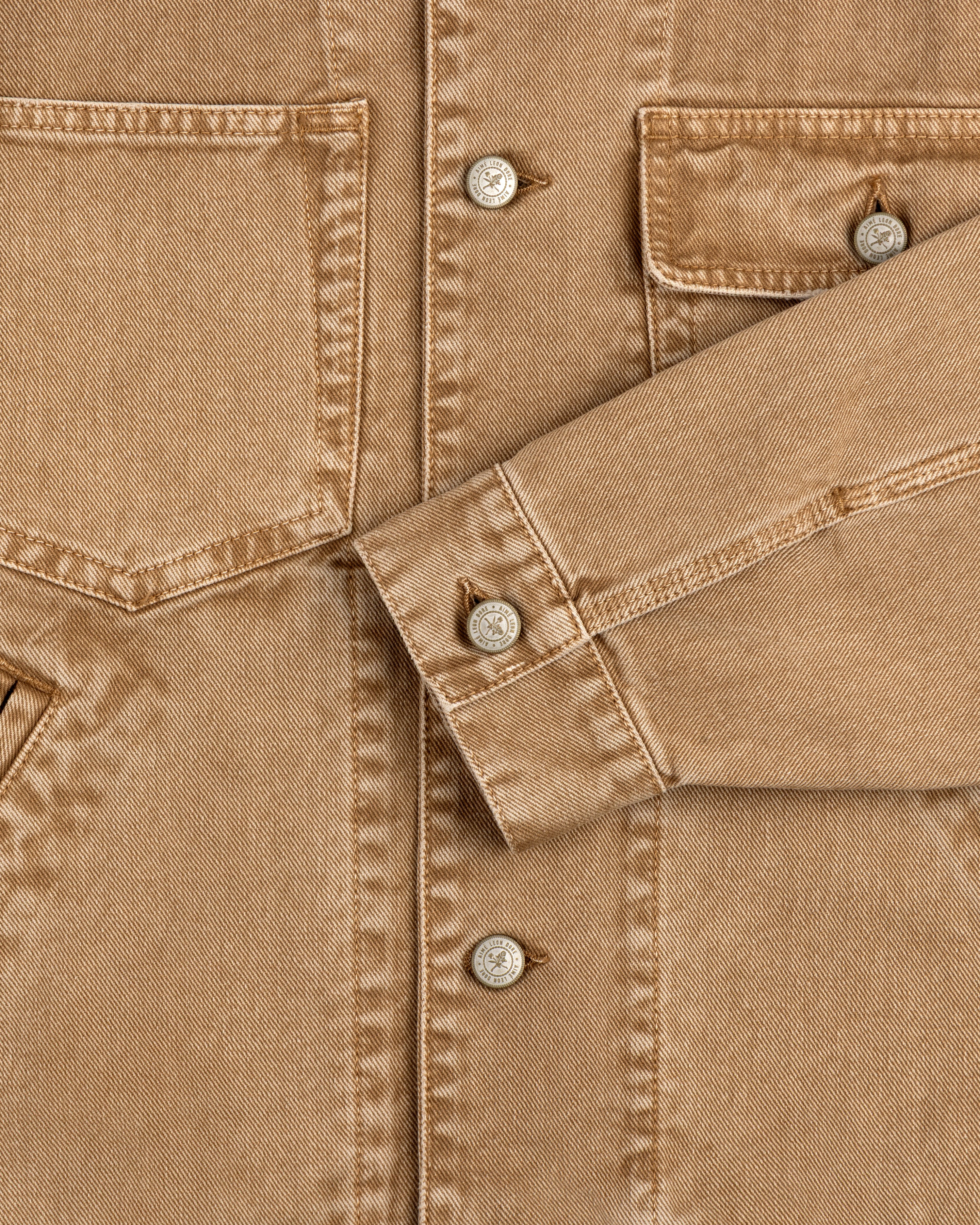 Close-up of a Denim Trucker Jacket highlighting tan fabric, buttons, breast pockets, and detailed stitching.