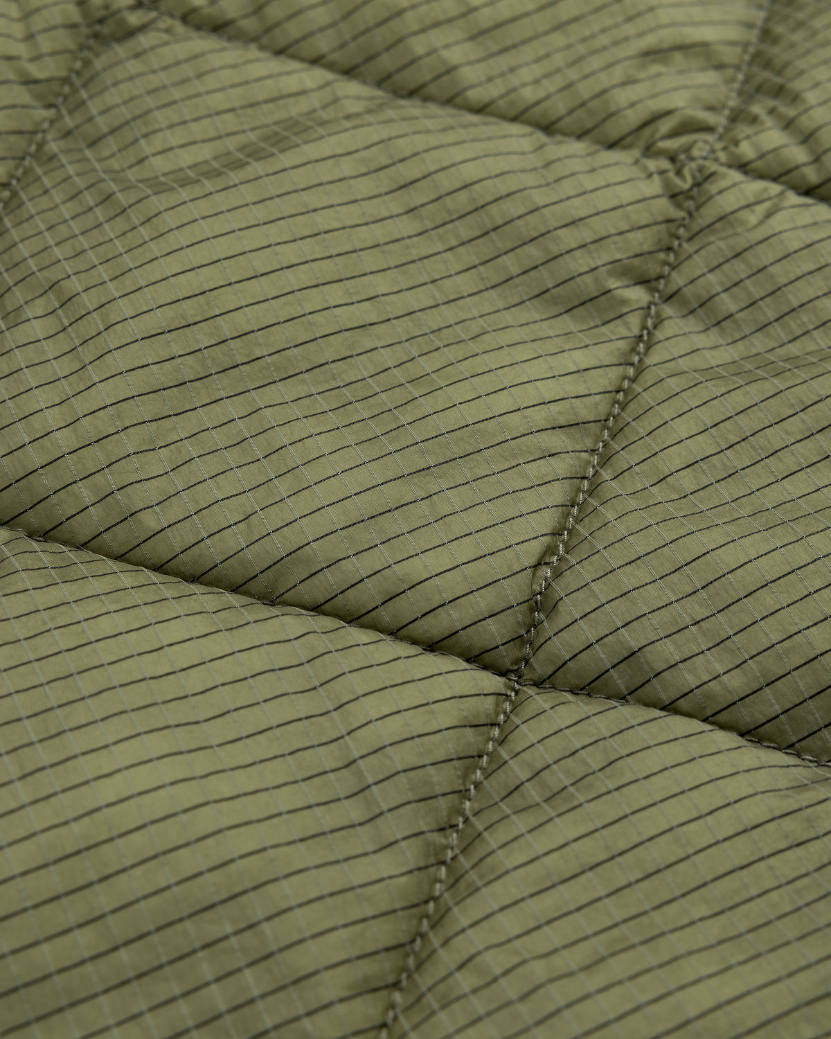 Close-up of Nylon Quilted Unisphere Jacket in olive green with square grid and visible stitching.