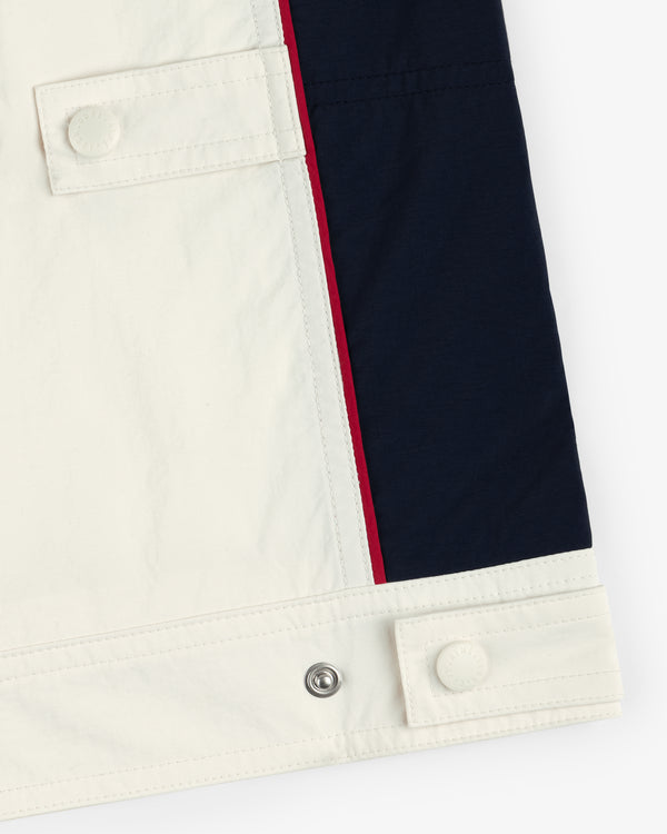 Close-up of Nylon Moto Jacket's hem with white, navy, and red color blocks, buttons, and snap fasteners.
