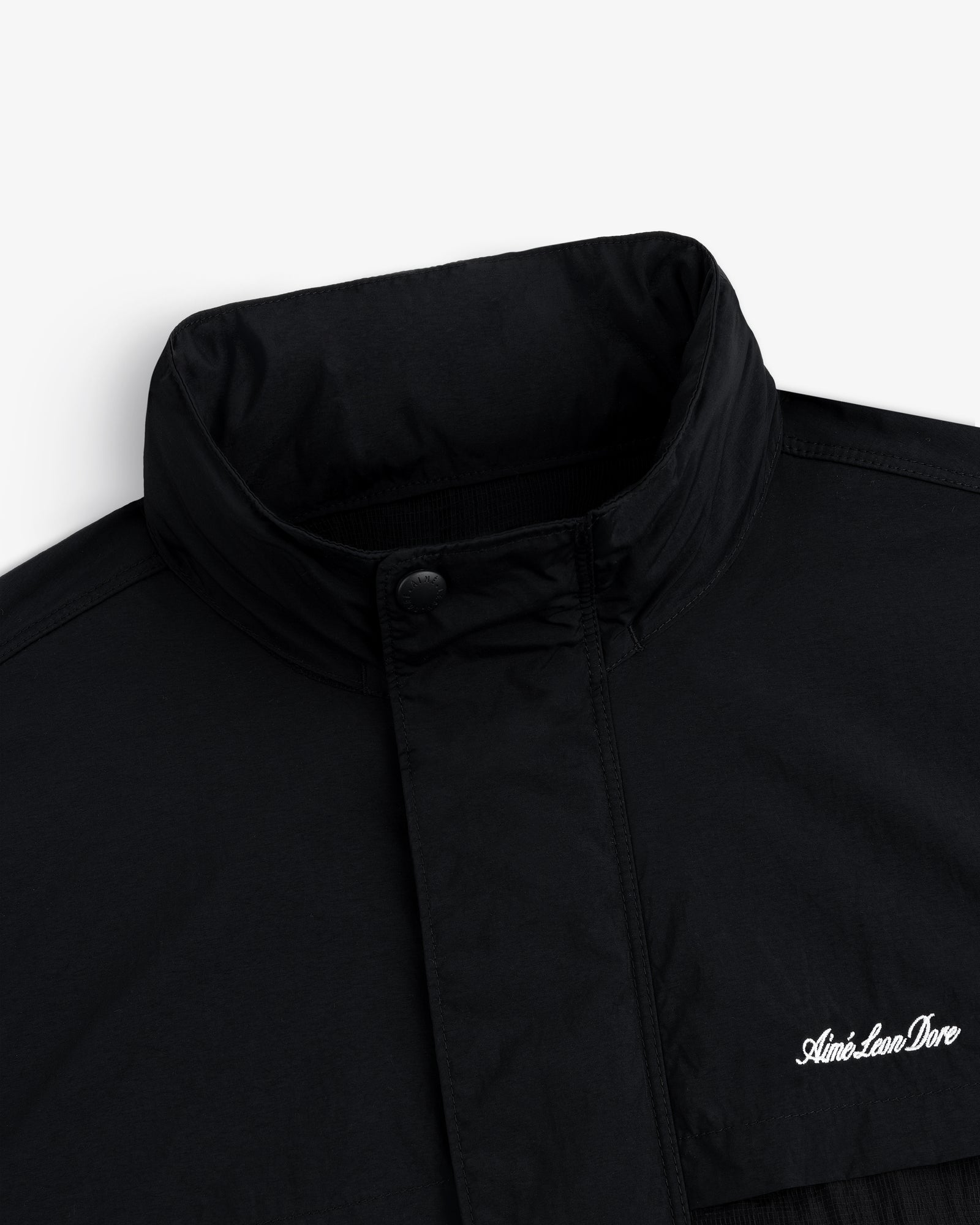 Close-up of a black Nylon Track Jacket with a high collar and "Aint-Lion-Dive" embroidered in white on the chest.