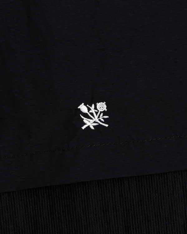 Small white embroidered rose with leaves on black Nylon Track Jacket, near the hem.